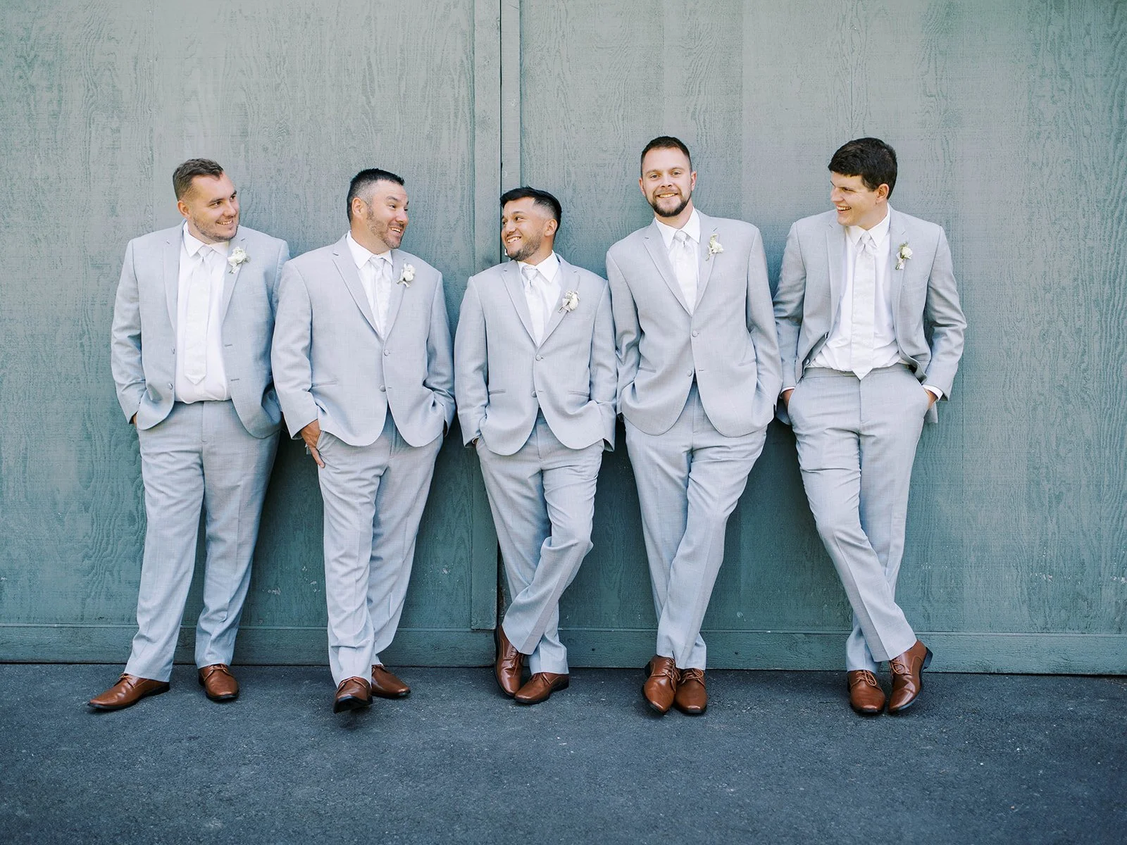 Groomsmen in matching gray suits posing together against textured blue wall.