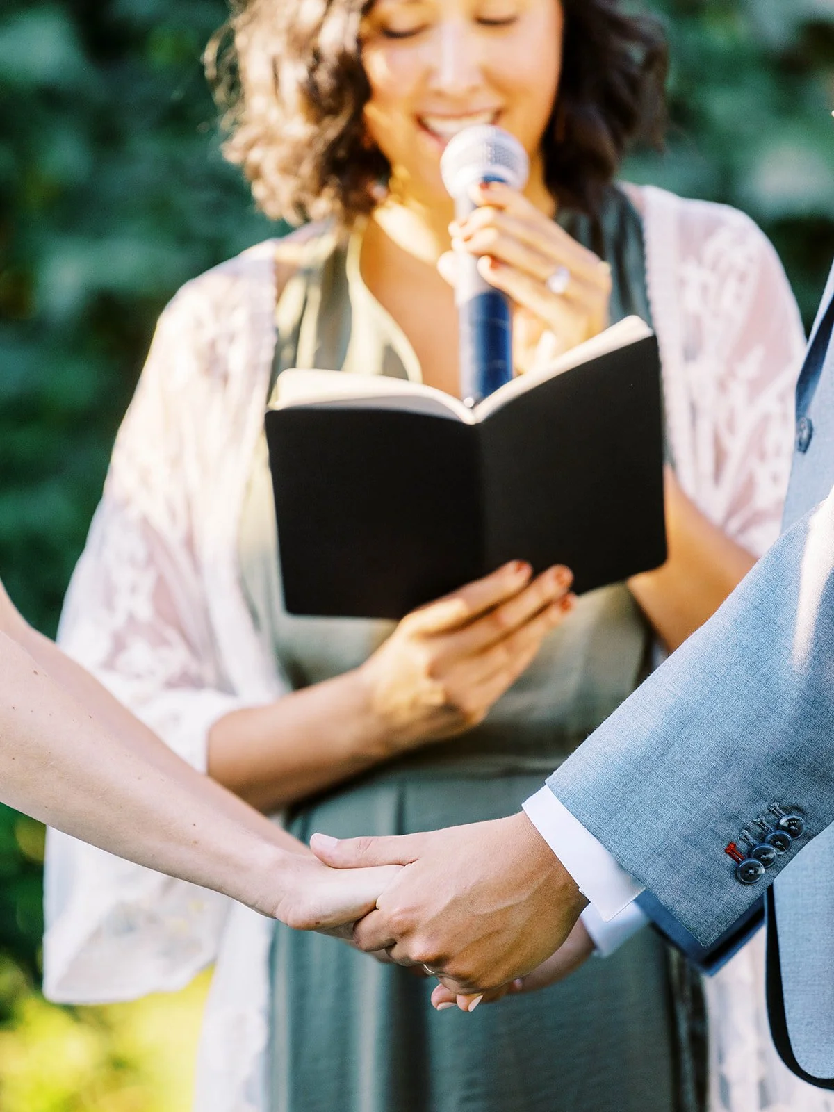 Close-up of couple holding hands during vows with officiant reading from book