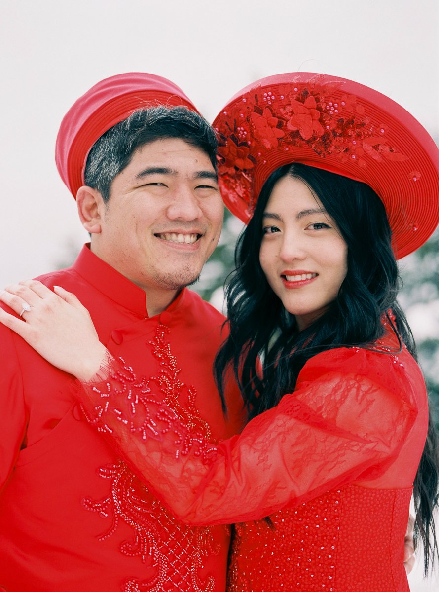 Couple smiling together in red Vietnamese áo dài during snowy Mount Hood engagement session.