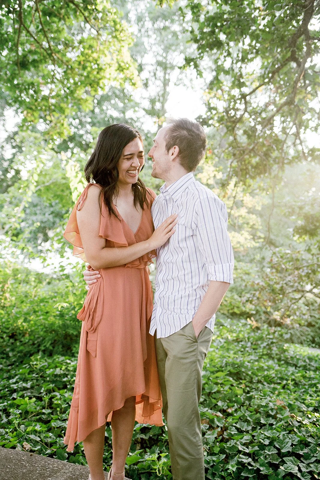 Couple laughing together in golden hour light surrounded by greenery during engagement session