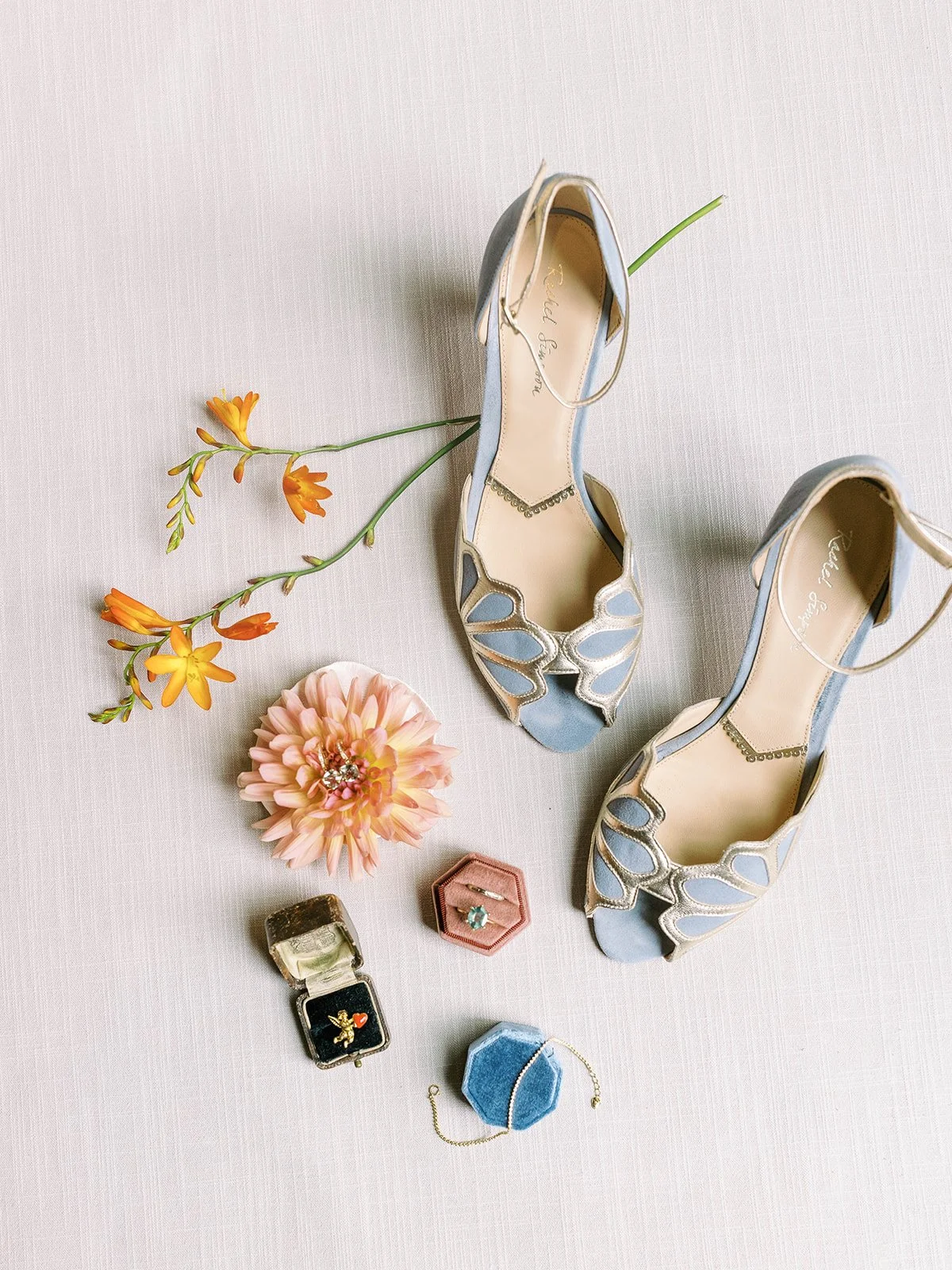 Blue bridal heels with rings, bracelet, and flowers styled on neutral linen background