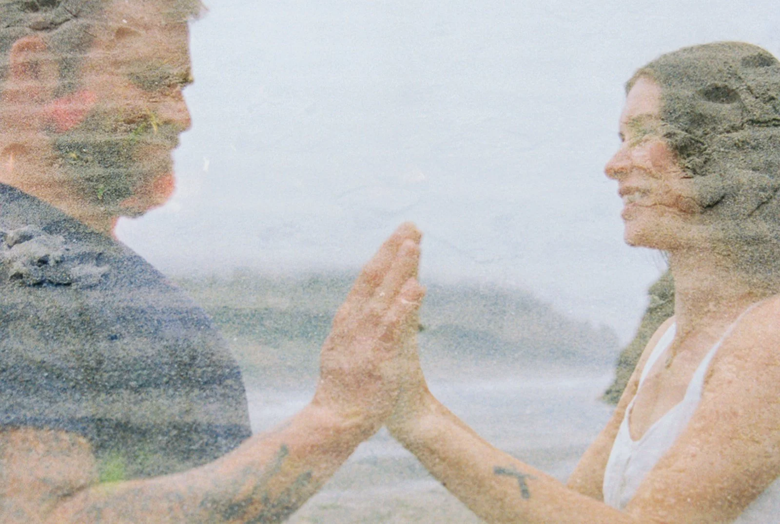 Artistic double exposure of couple touching hands with beach texture layered over soft ocean backdrop.
