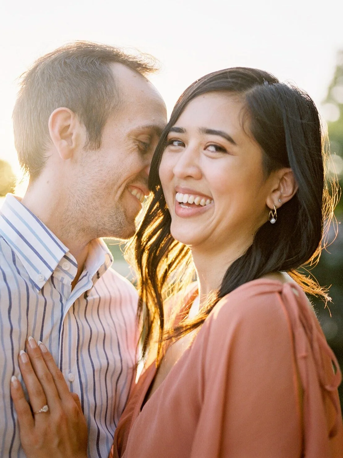Couple laughing together beside a lake in warm golden light during their engagement session.