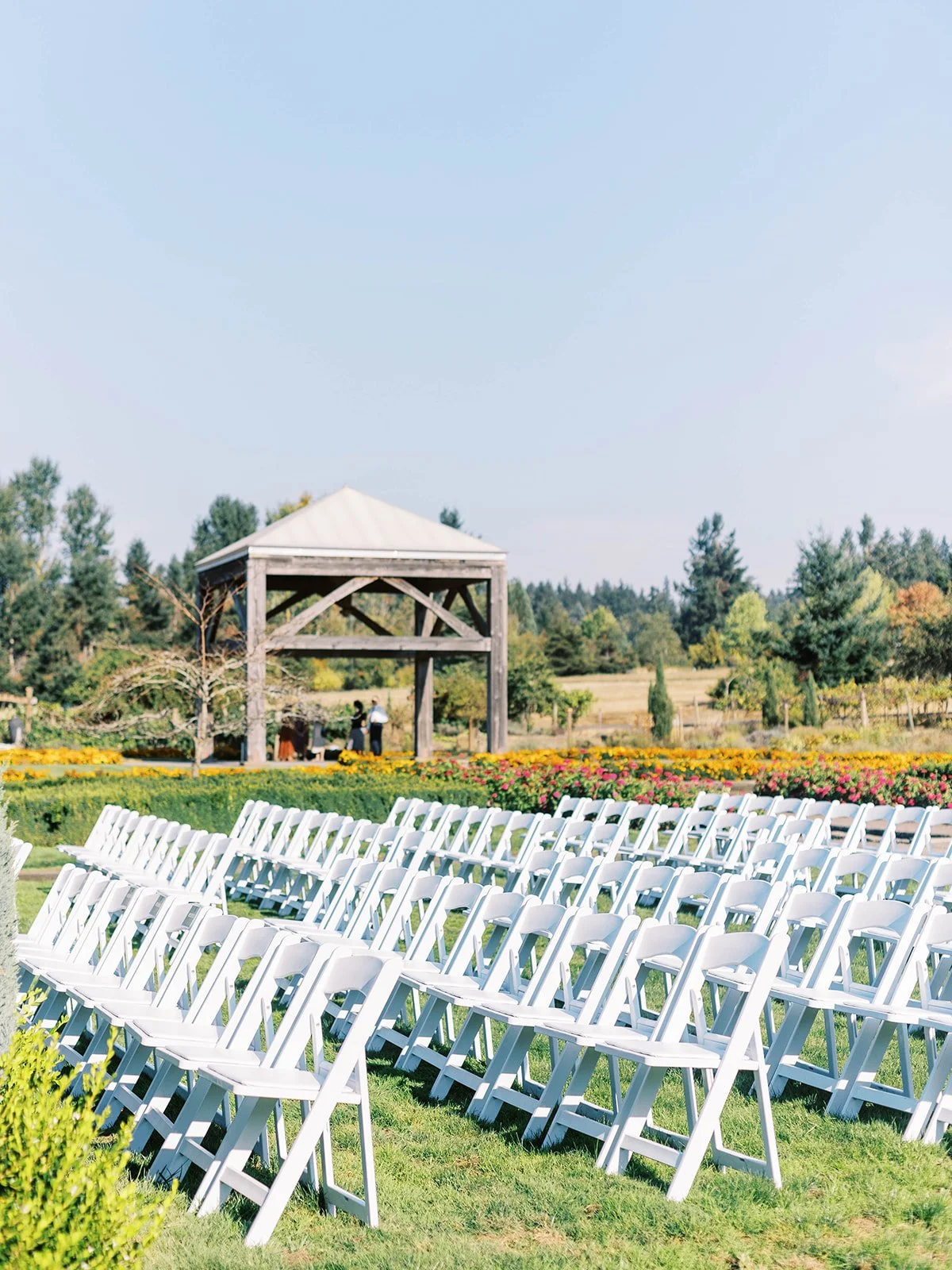 Rows of white ceremony chairs arranged on a lawn facing a wooden garden pavilion.