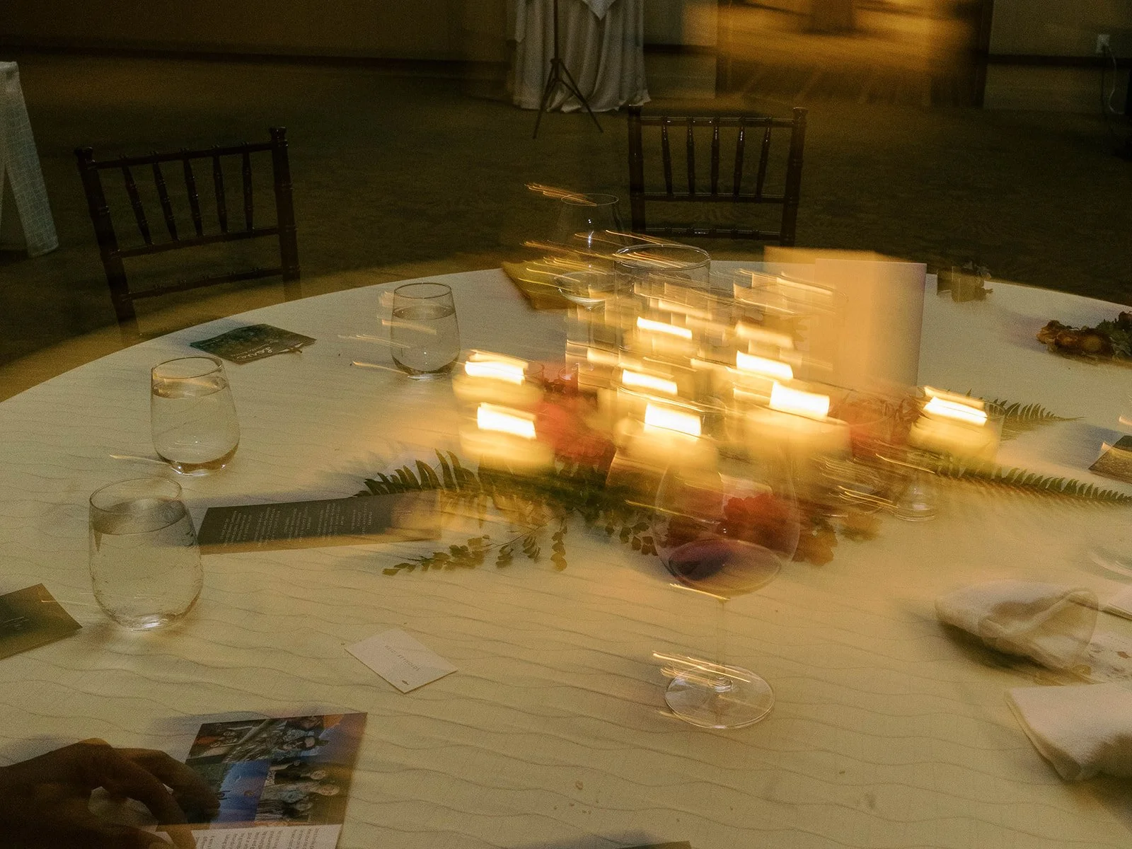 Long-exposure artistic shot of a reception table with candles glowing and motion blur, guests' books and glassware visible in the warm light