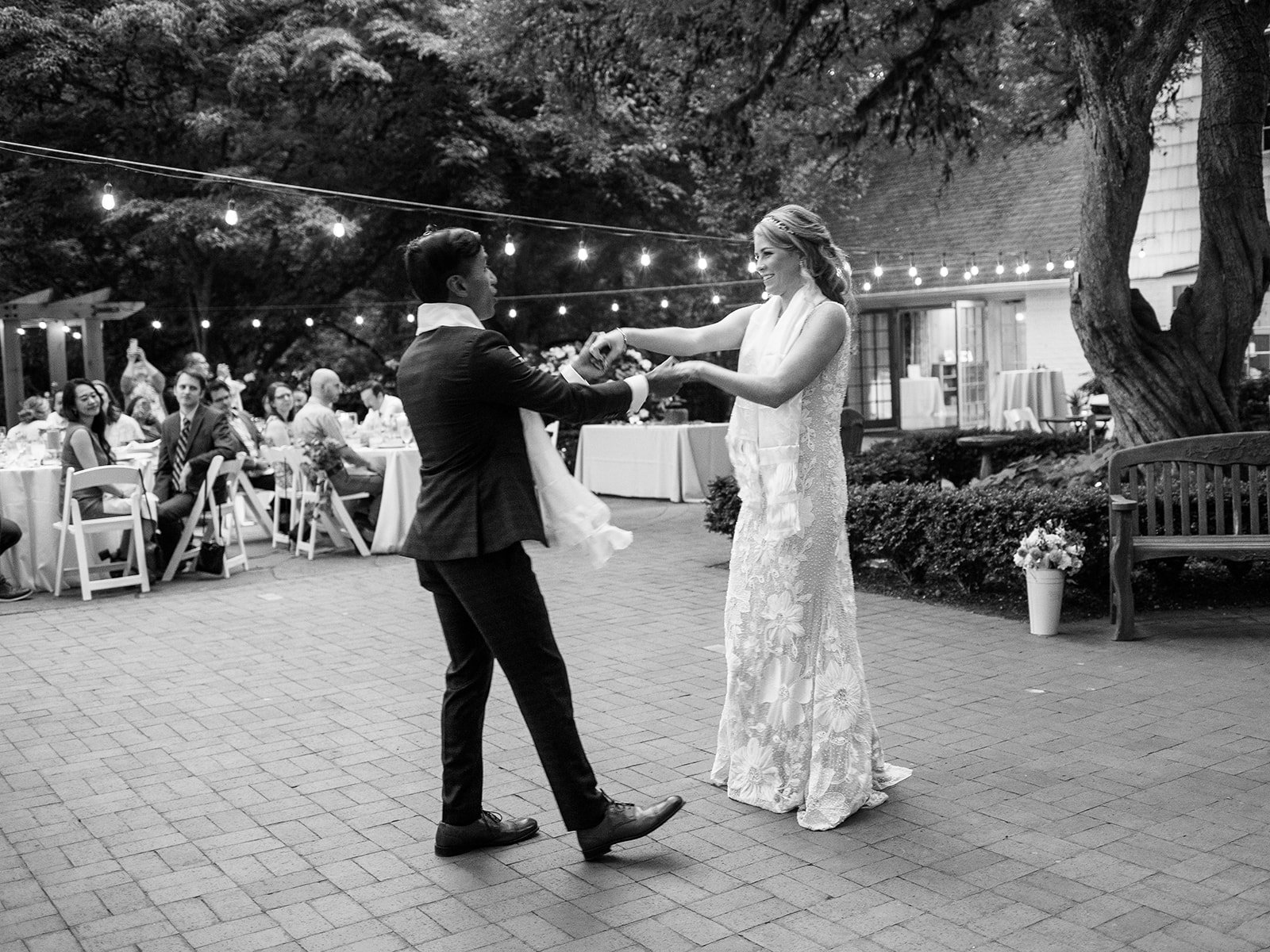 Black-and-white photo of the newlyweds twirling during their outdoor garden reception.
