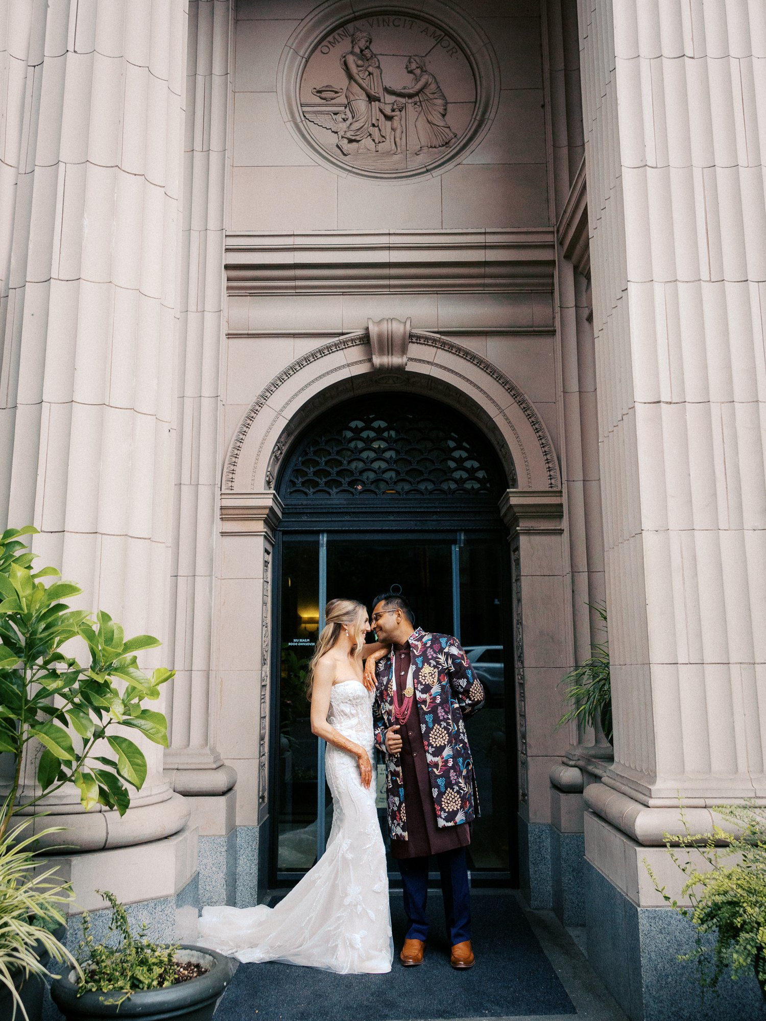 Alacia and Rohit pose together beneath the ornate columns and arched entrance of Portland’s Sentinel Hotel.