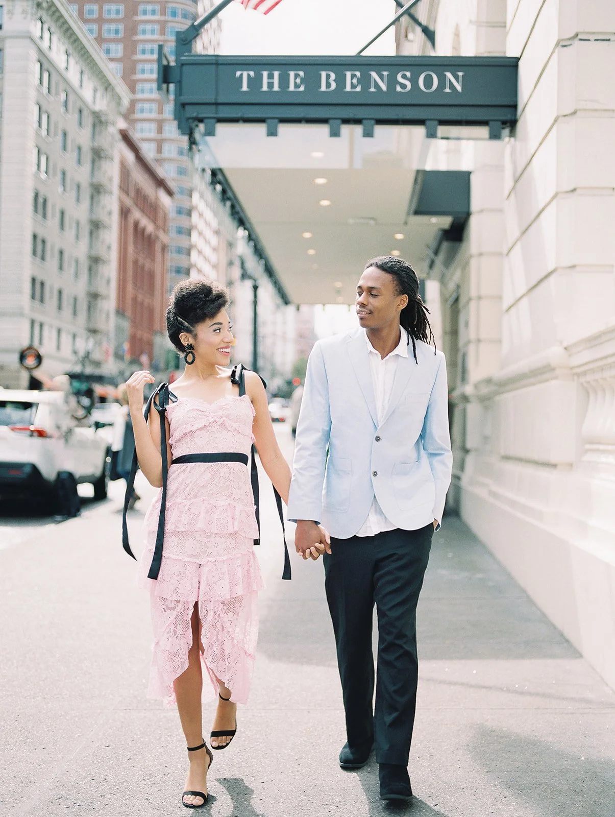 Couple walking hand in hand along sidewalk near The Benson Hotel in Portland