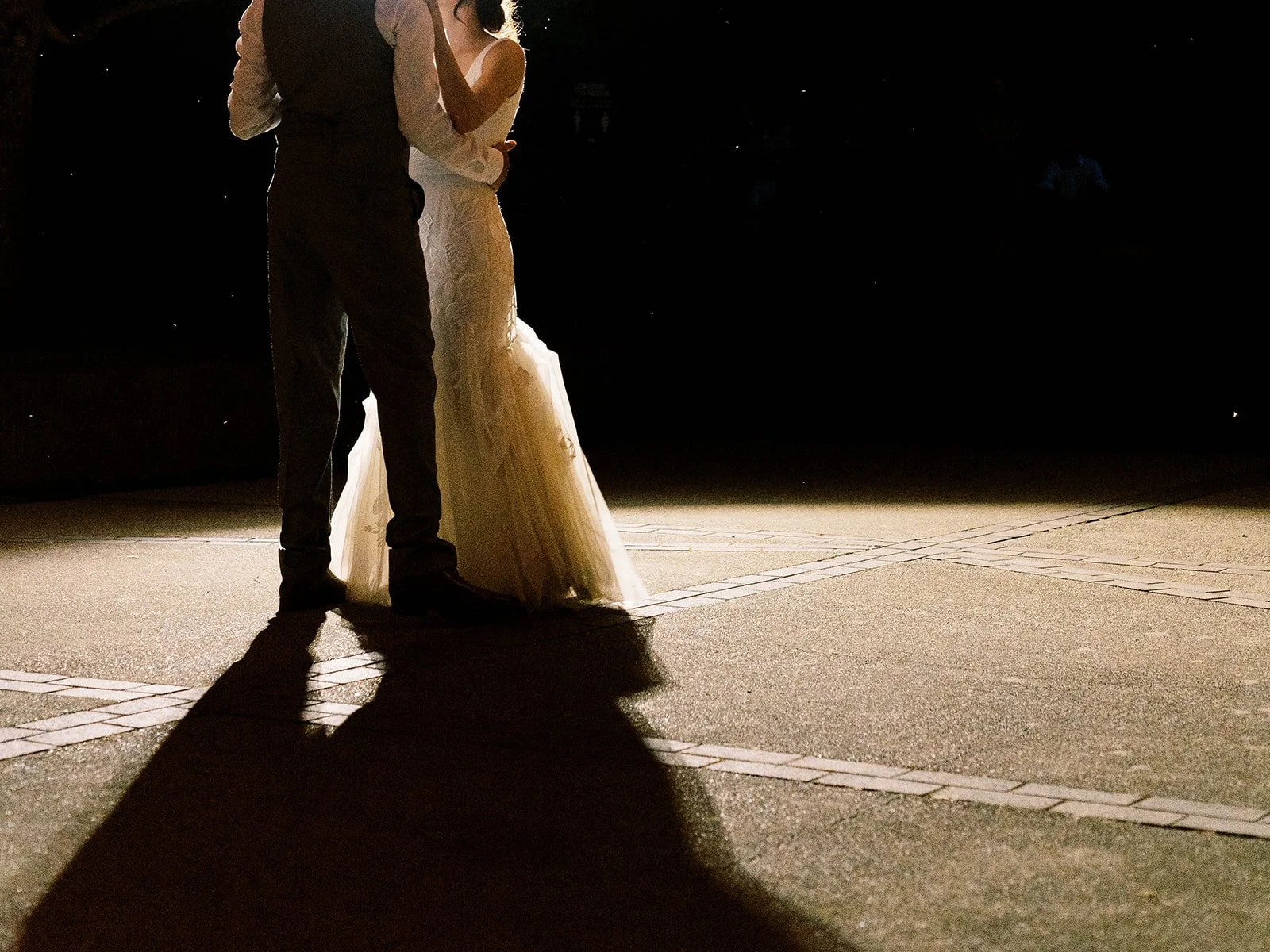 Close-up of bride and groom dancing at night with long shadows cast on the ground