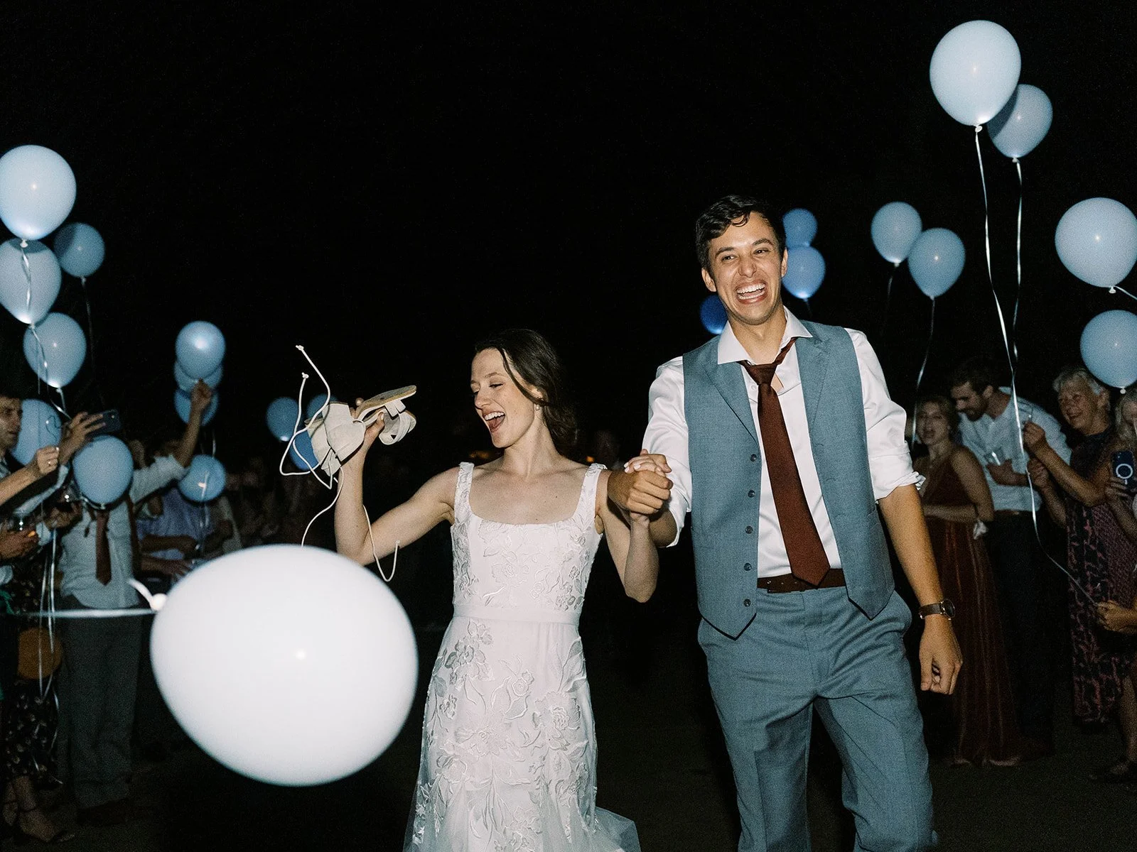 Bride and groom walking through guests holding white balloons during wedding send-off