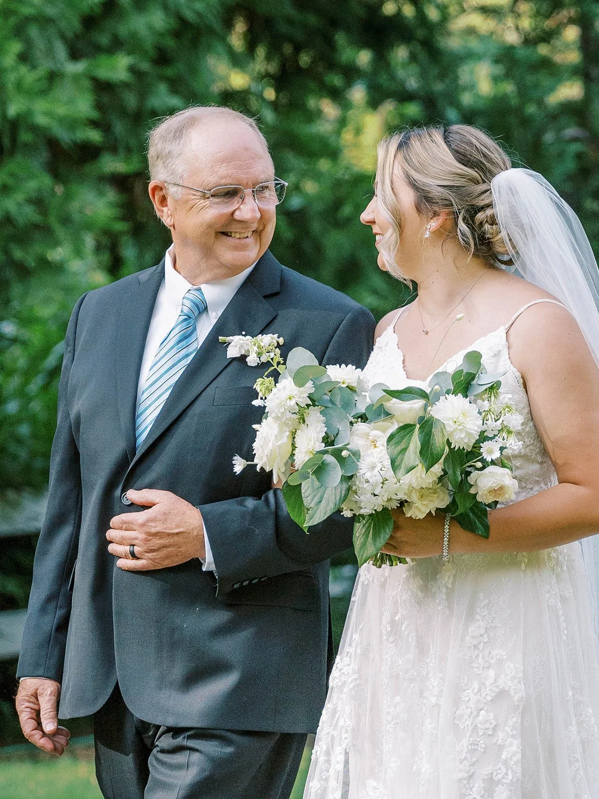 Close portrait of bride walking arm in arm with her father, holding white bouquet before ceremony.