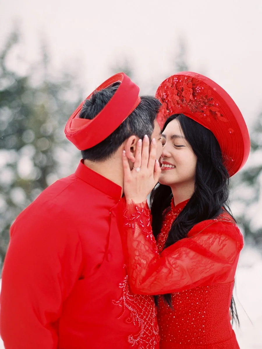 Close-up of couple in red attire sharing a kiss in falling snow at Mount Hood.