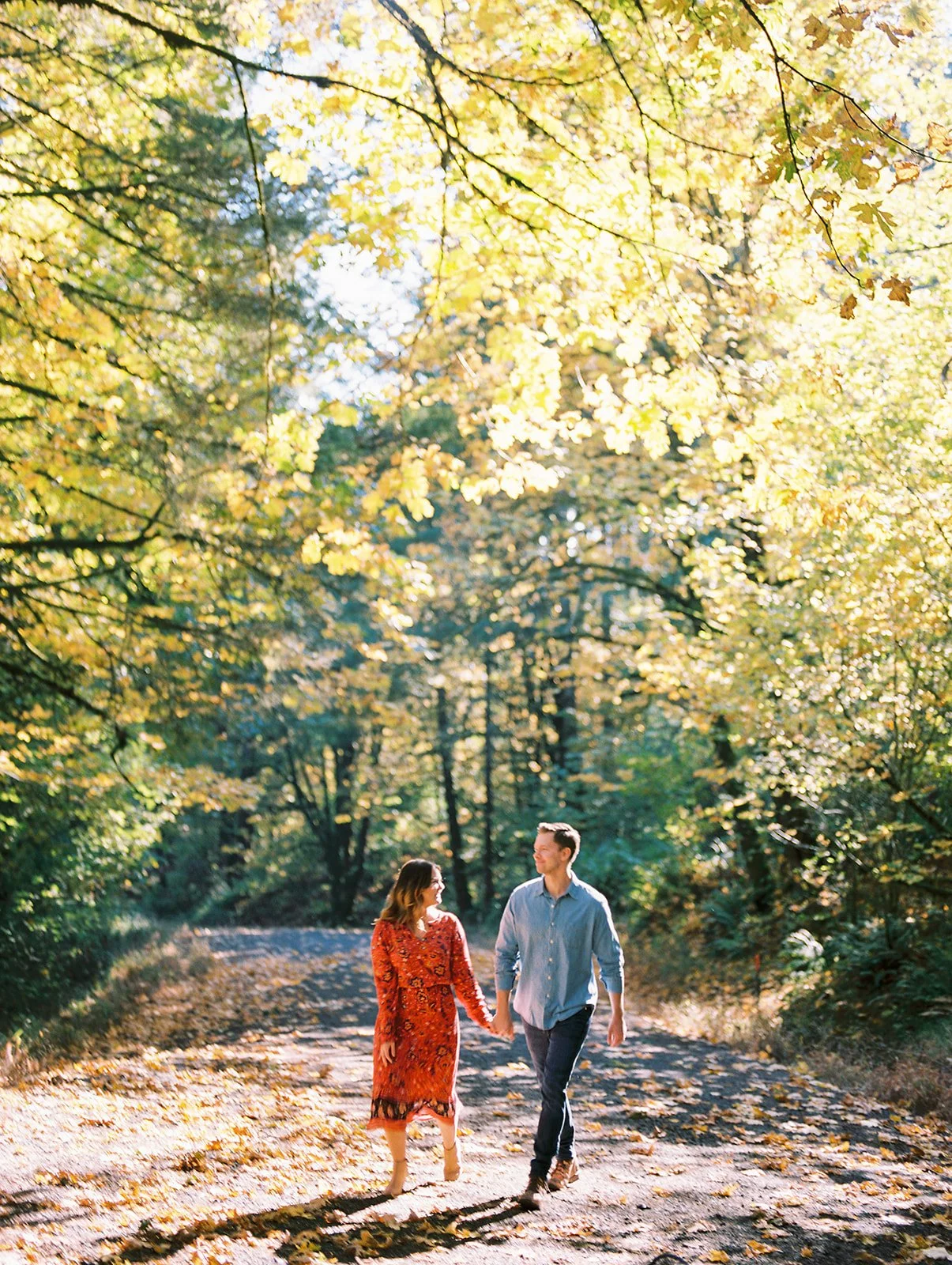 Couple holding hands walking along a tree-lined path with golden fall foliage in Oregon