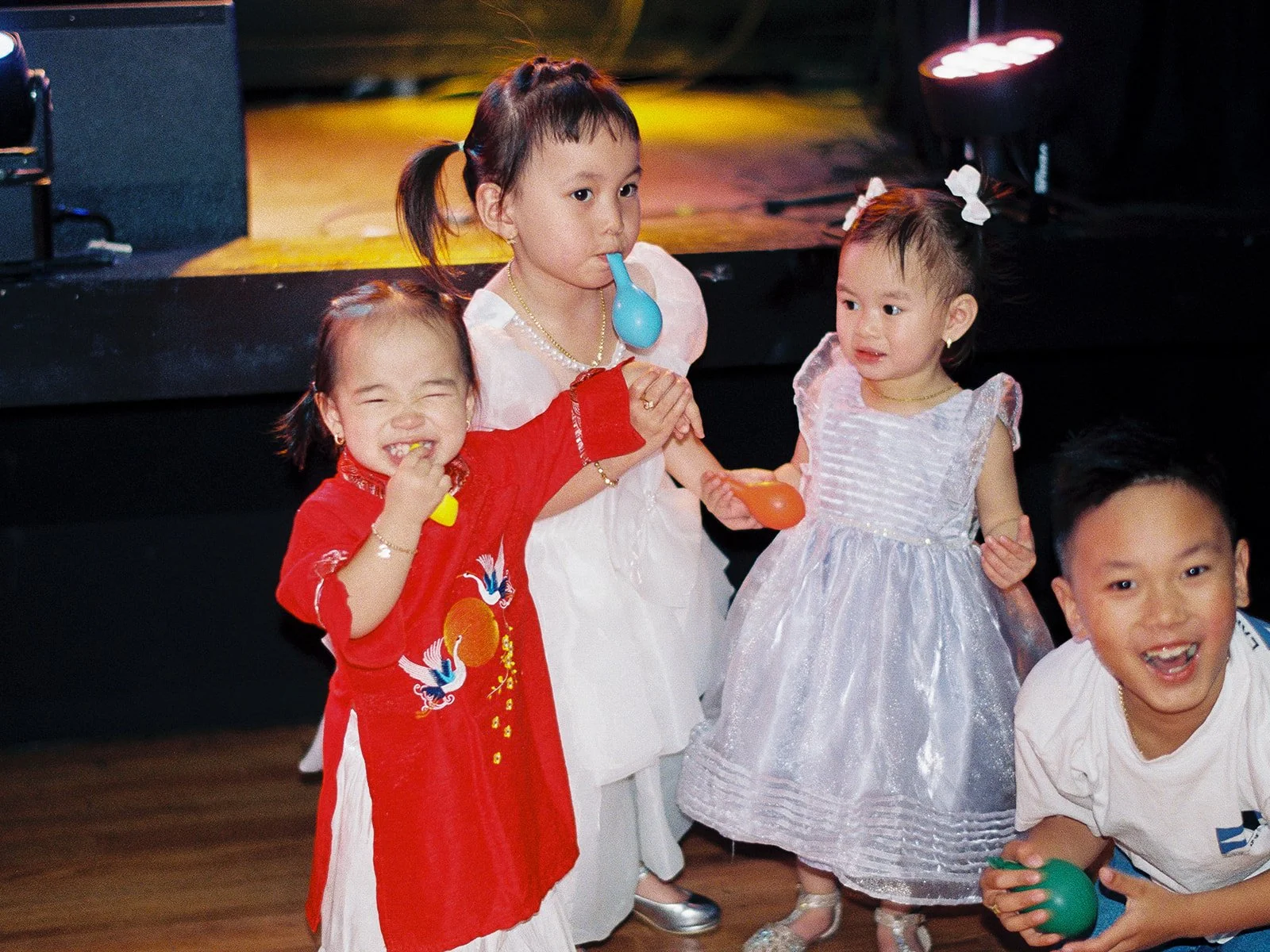 Four young children — including a girl in a red áo dài and a toddler in a sparkly dress — playing with party favors on the dance floor at the Mekong Bistro reception
