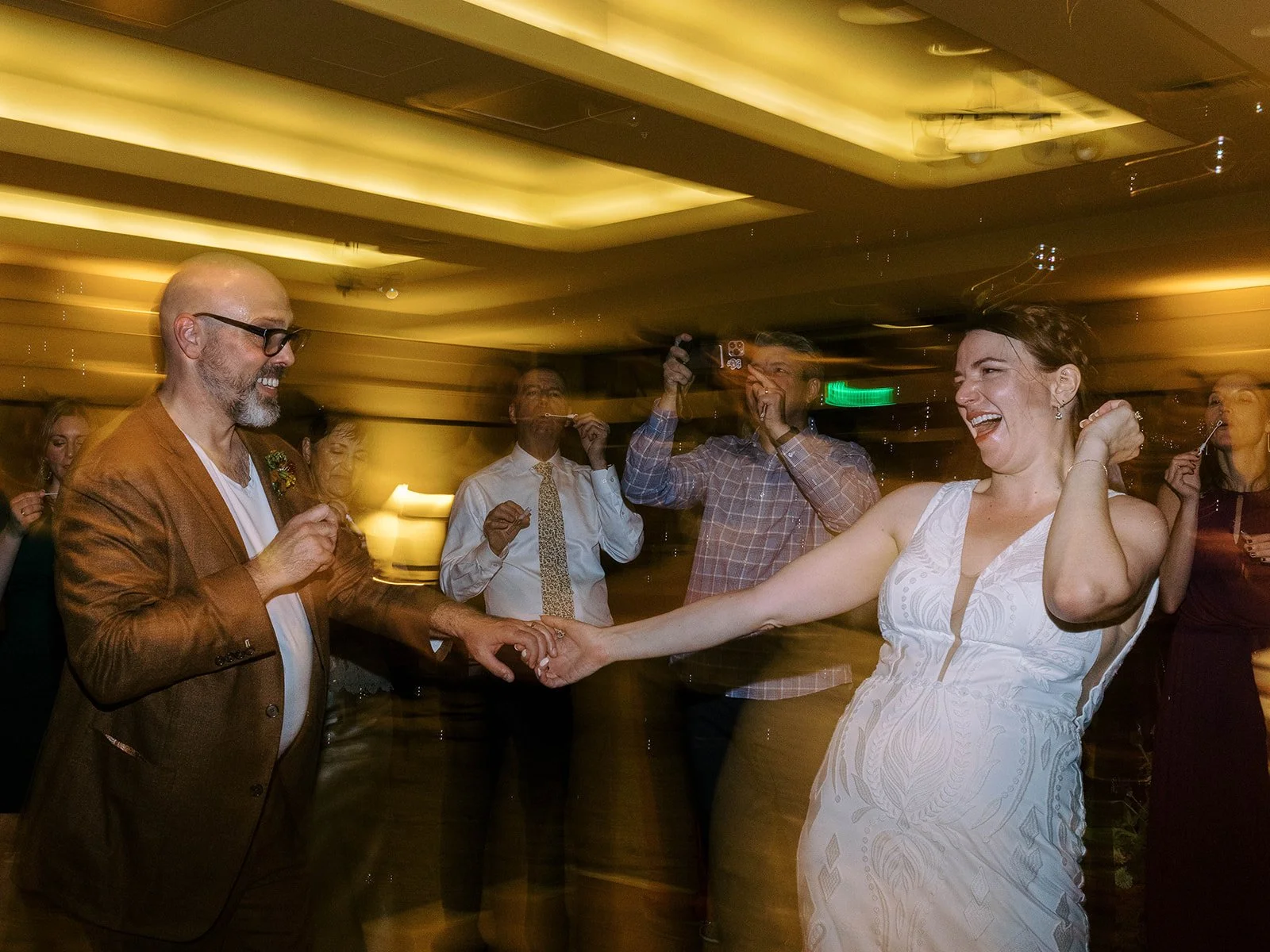 Bride and groom holding hands and dancing as guests blow bubbles around them at the reception.