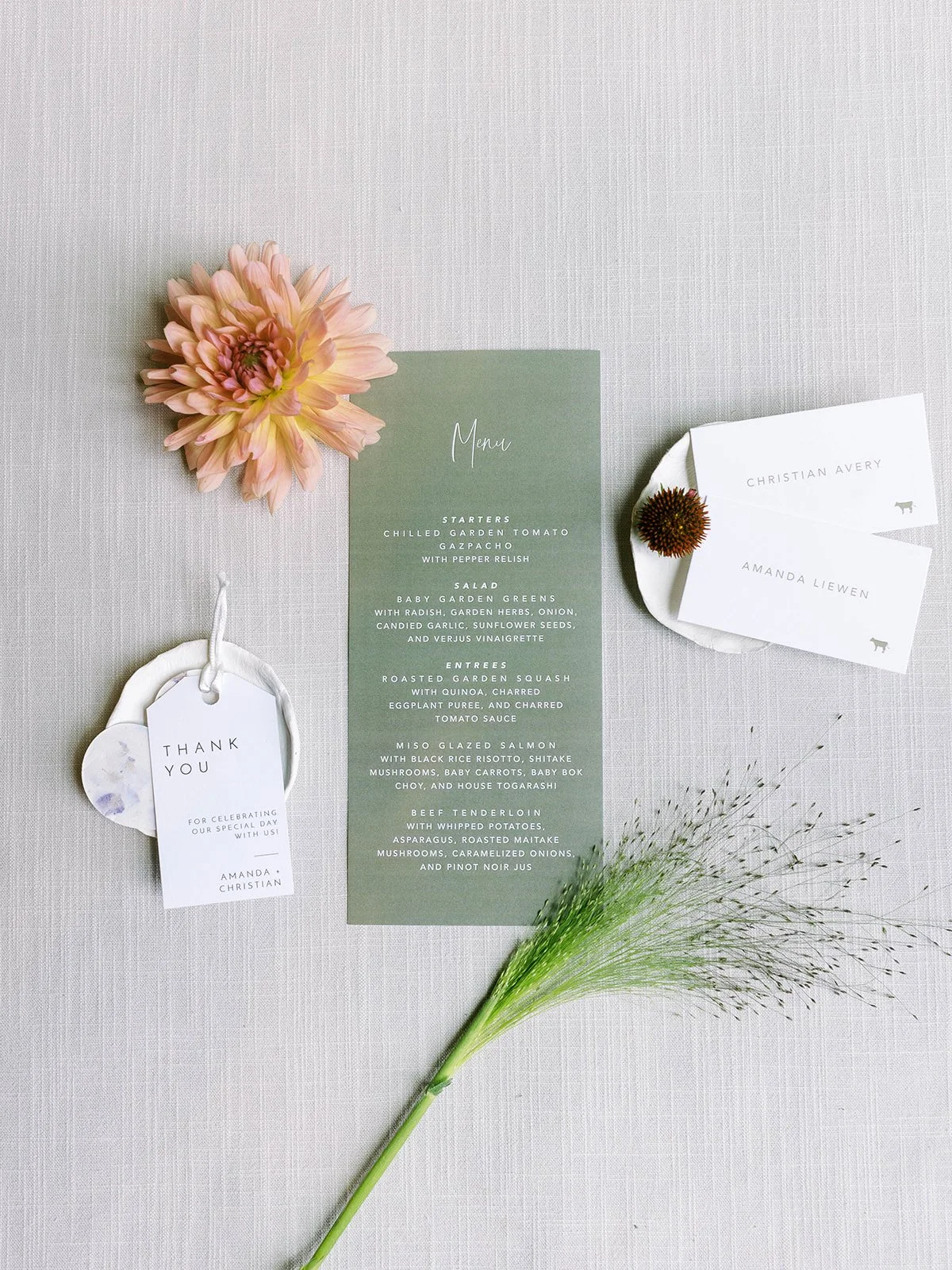 Flat lay of wedding stationery including menu, name cards, and floral accents on a neutral textured background.
