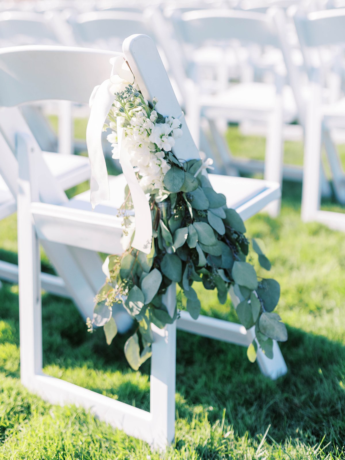 White flowers and eucalyptus tied to a white ceremony chair at an outdoor Oregon garden wedding.