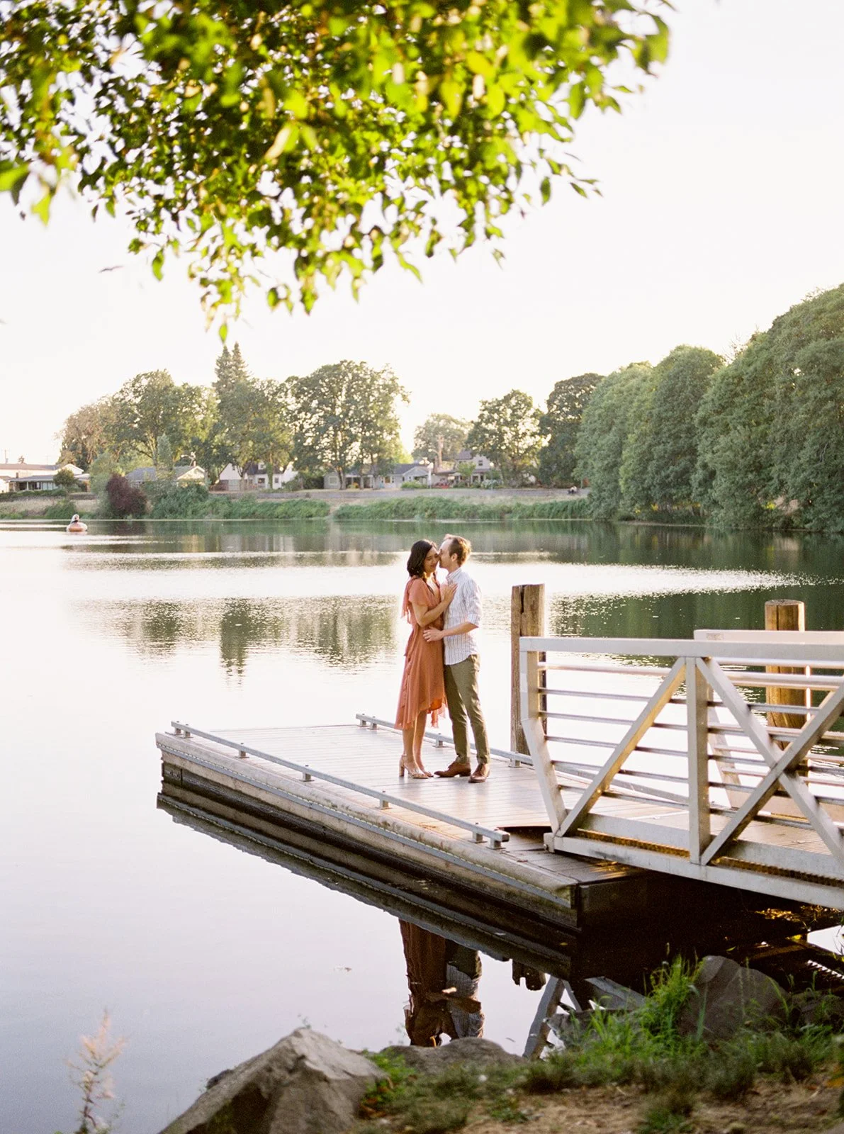 Couple on a dock at sunset, reflected in calm water during Oregon lakeside engagement session
