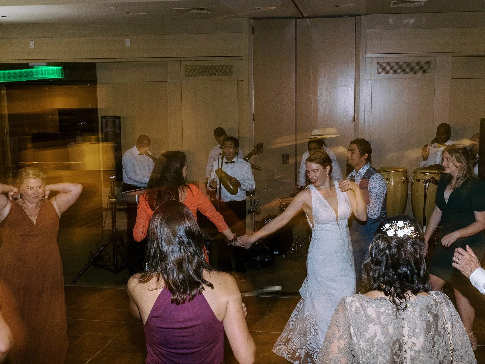 Bride dancing exuberantly with guests surrounding her on the floor, live band performing in the background