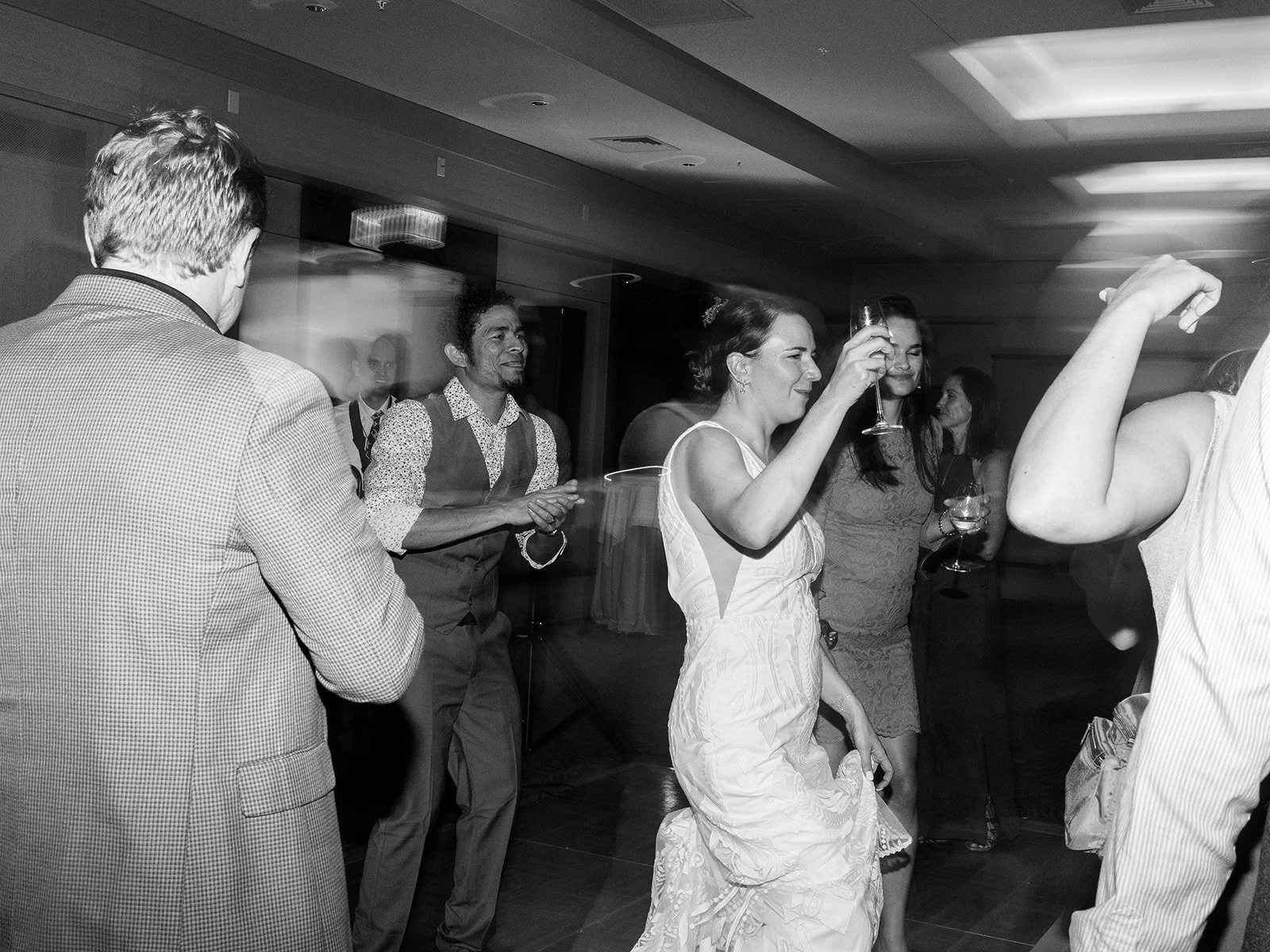 Black and white photo of the bride dancing with a champagne glass raised, surrounded by guests on the lively dance floor