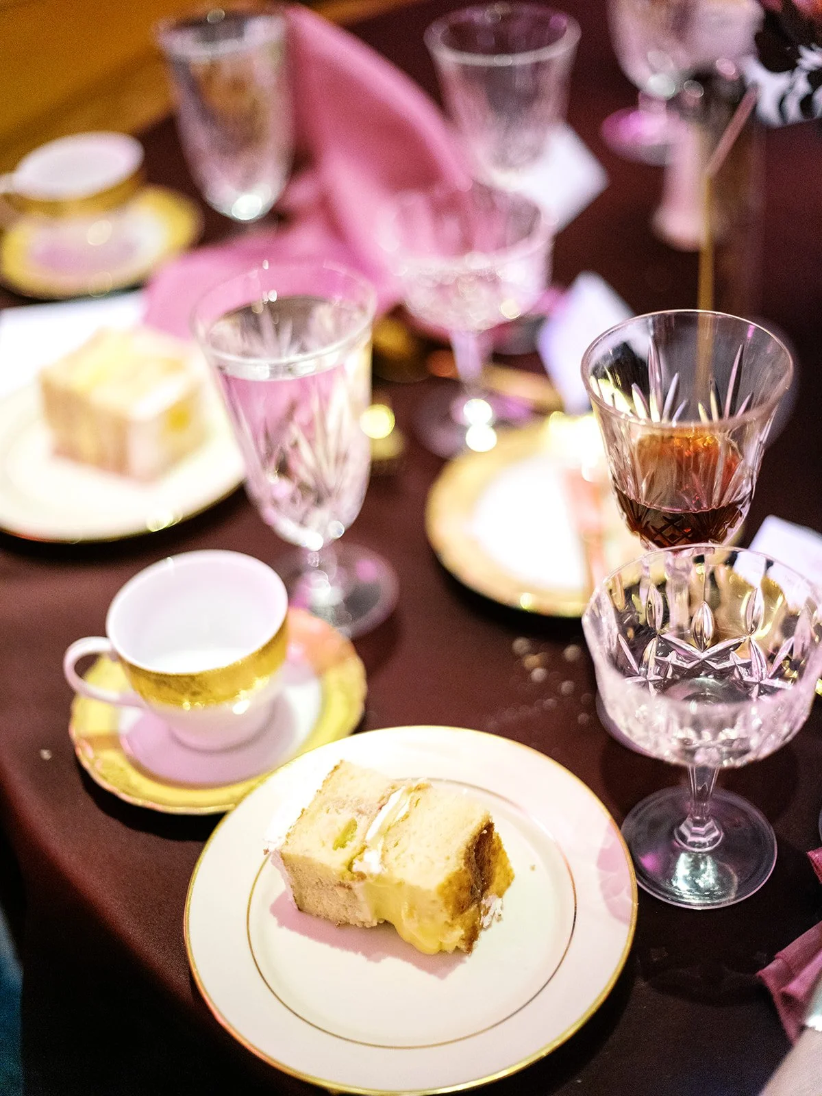Close-up of plated wedding cake slice with custard filling on table with crystal glassware and pink napkins.