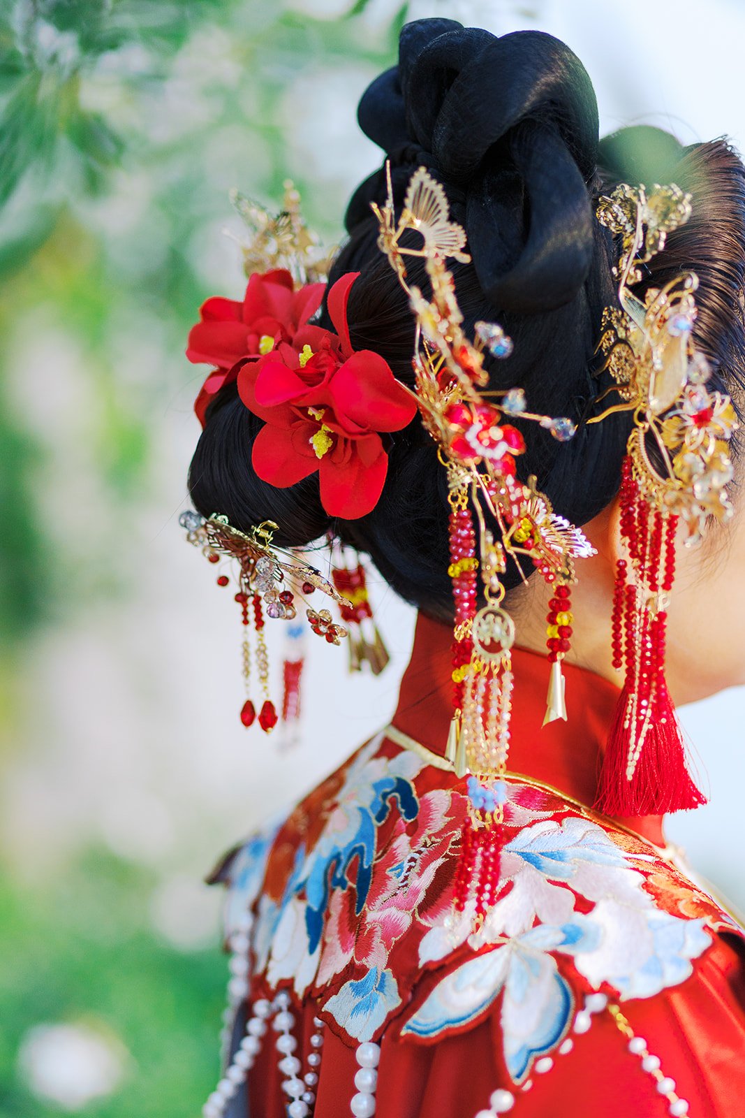 Close-up of intricate bridal hairstyle with red flowers and gold hairpins adorned with beads and tassels
