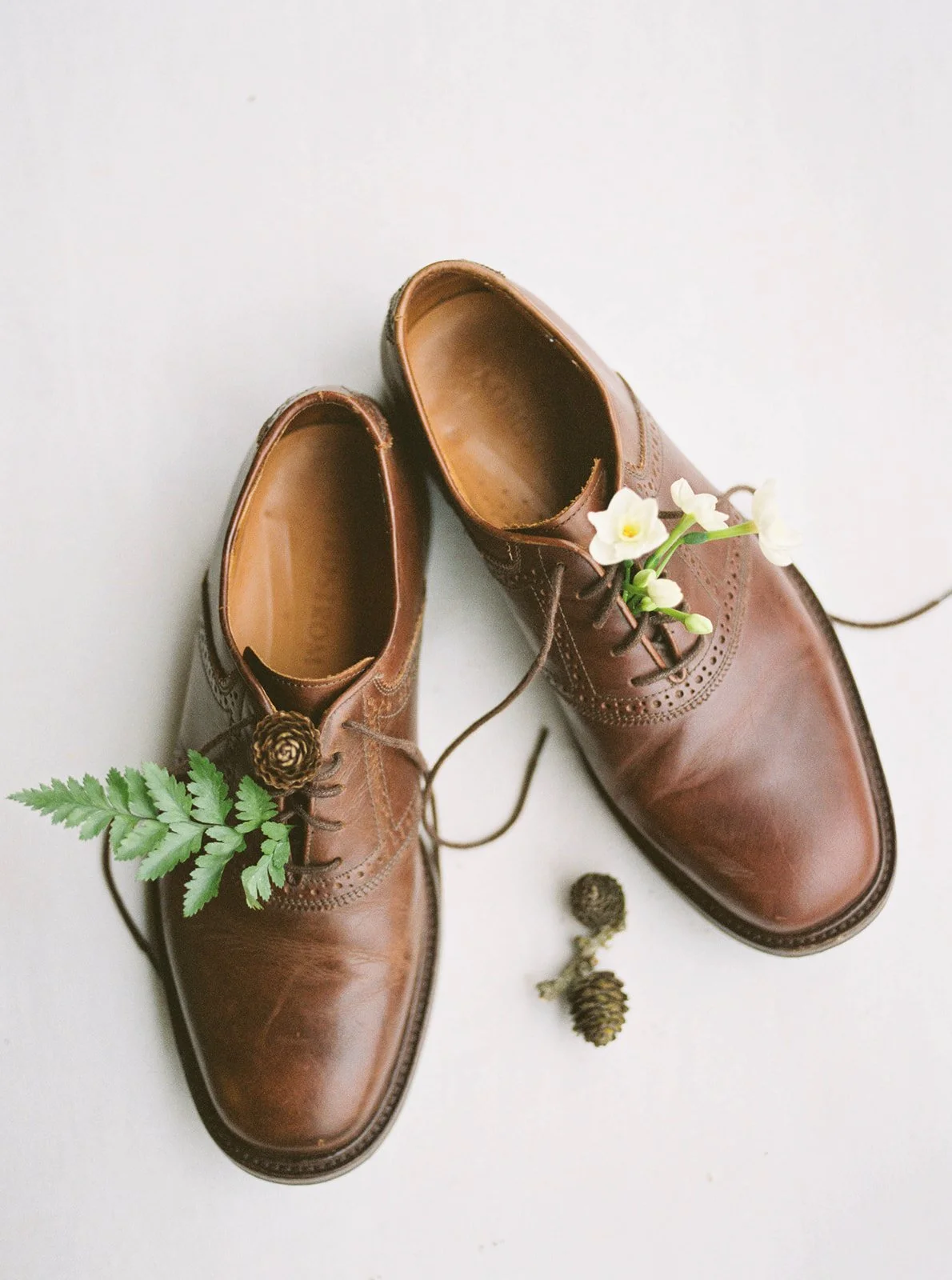 Brown leather groom’s shoes styled with fern, white flowers, and pinecones for an Oregon wedding.