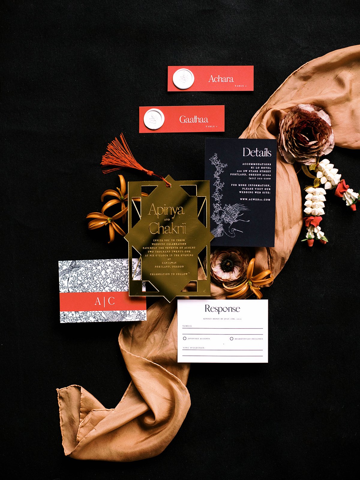Wedding invitation suite with red place cards, gold stationery, flowers and a jasmine garland.