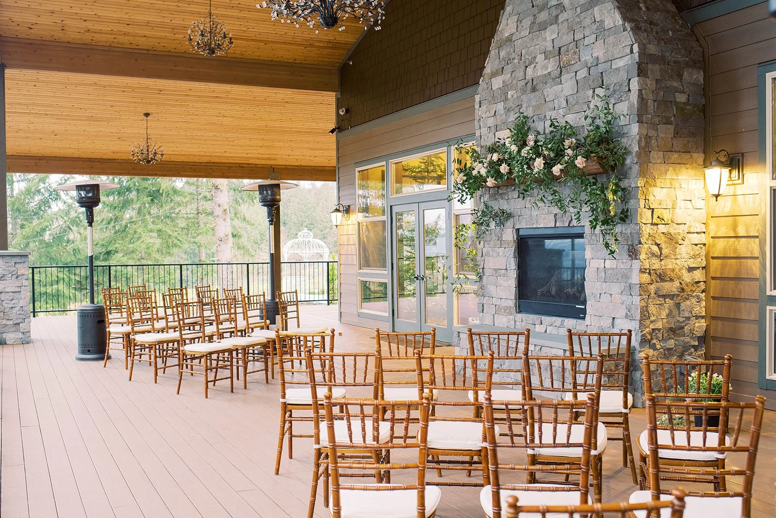 Intimate outdoor wedding ceremony setup with wooden chairs and a stone fireplace covered in flowers.