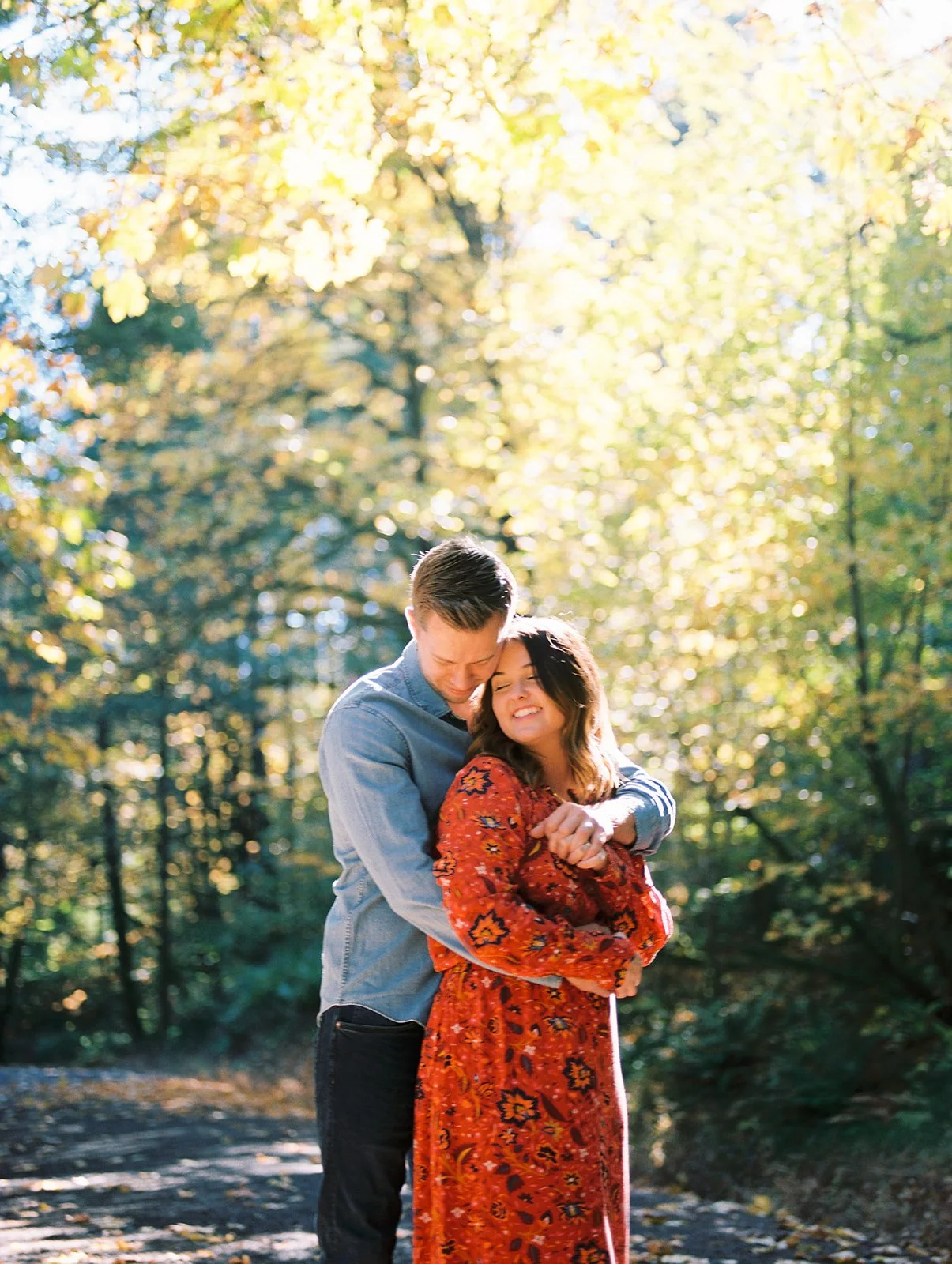 Man hugging woman from behind on a forest path with warm autumn light and colorful leaves