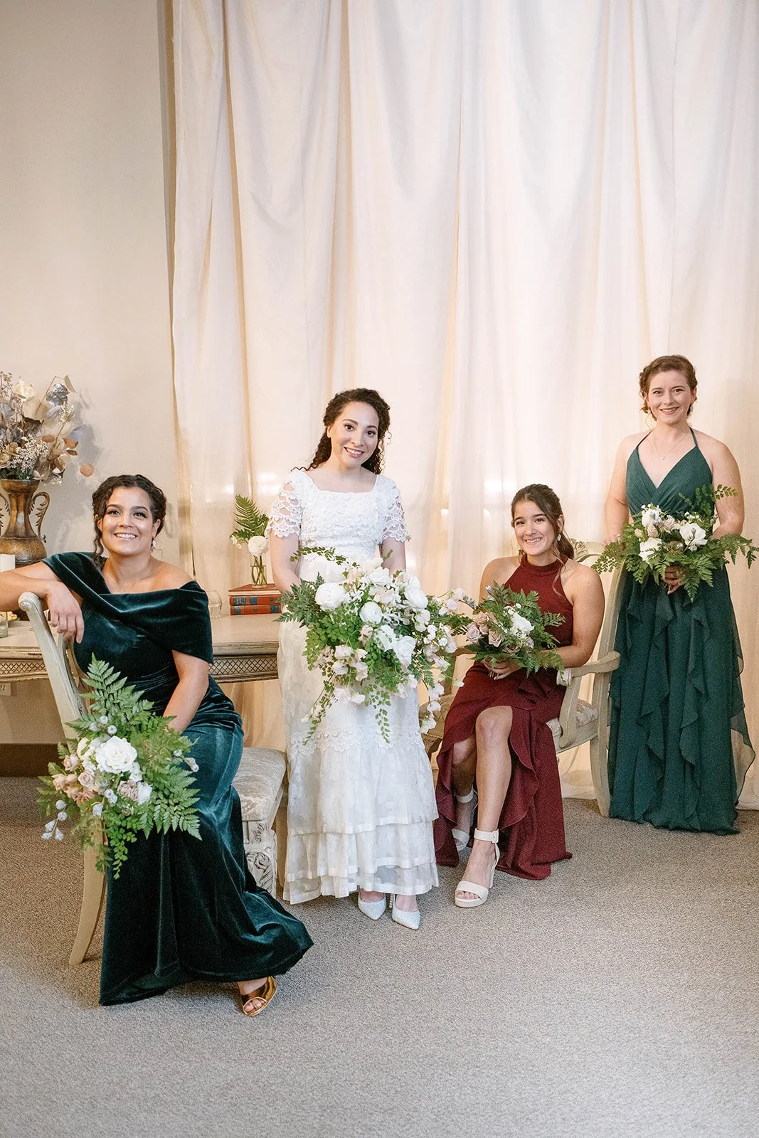 Bride with three attendants in jewel-tone dresses holding lush white and green wedding bouquets.