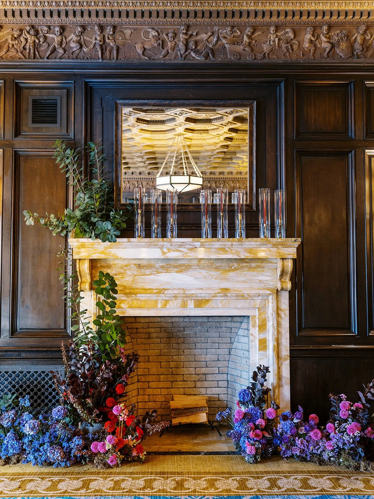 Marble fireplace decorated with greenery and vibrant florals in an elegant, wood-paneled room.