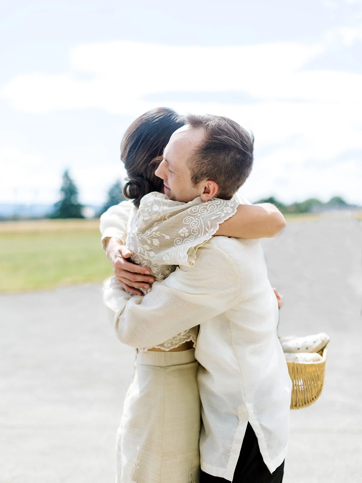 Bride and groom embracing warmly on the Pearson Airfield tarmac, bride holding a wicker basket
