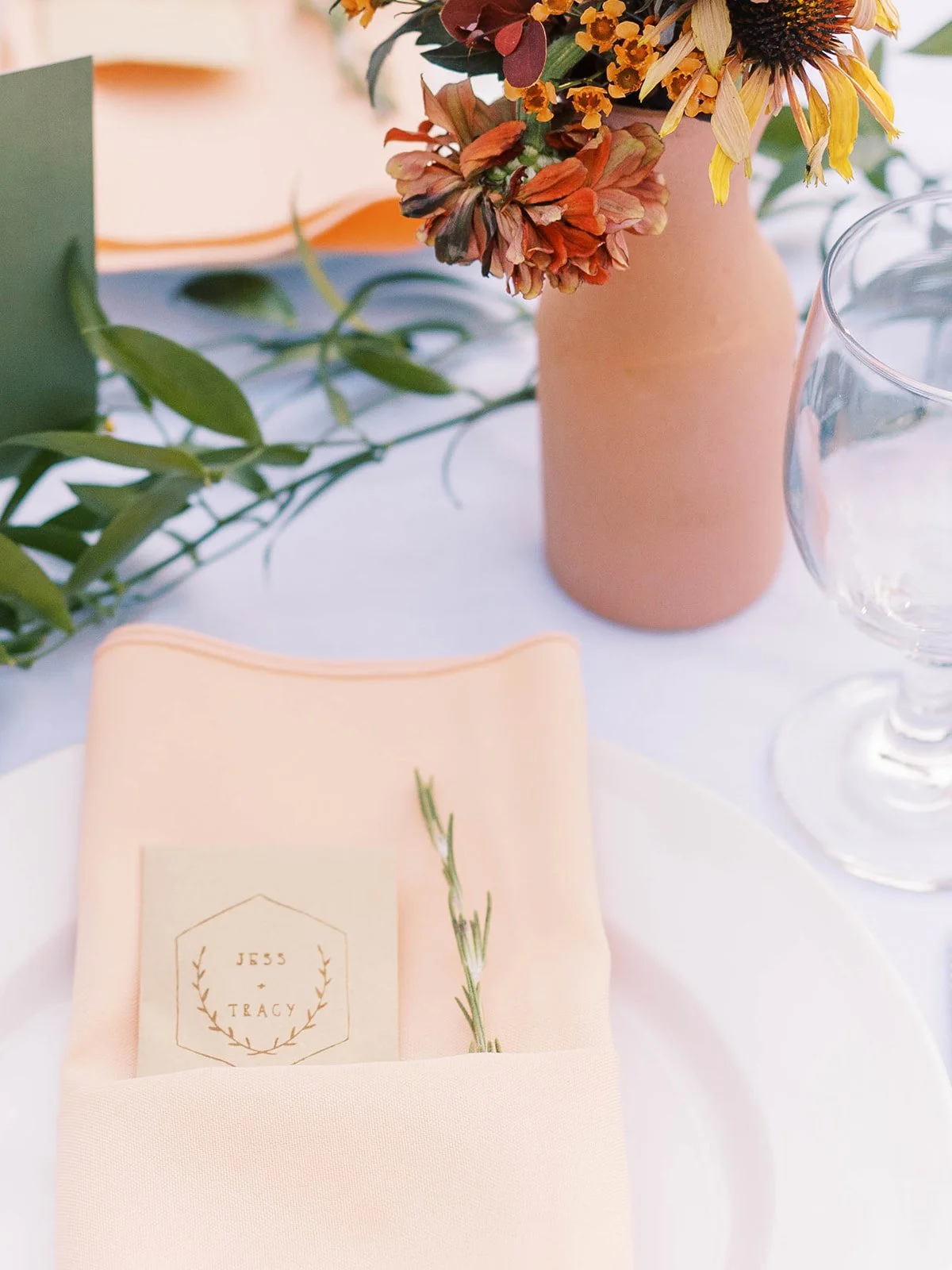 Peach wedding place setting with a personalized Jess and Tracy card beside warm-toned floral decor.
