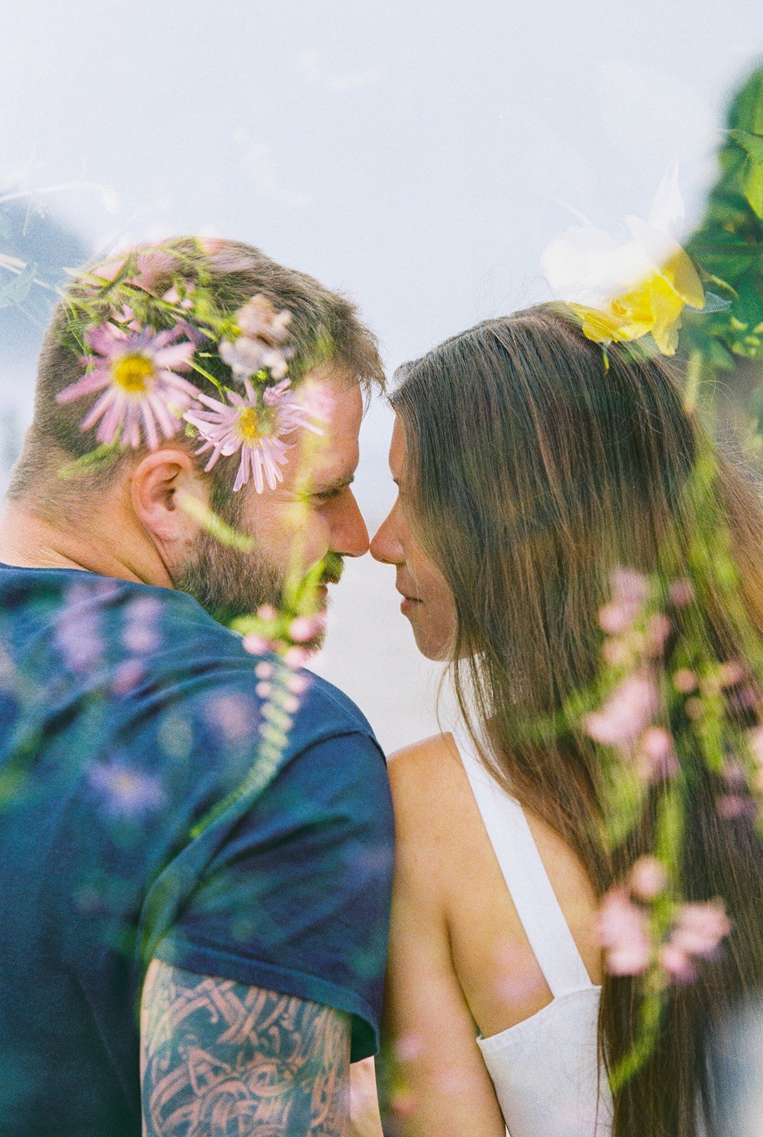 Close-up of couple leaning in forehead to forehead, with wildflowers layered in a dreamy double exposure effect.