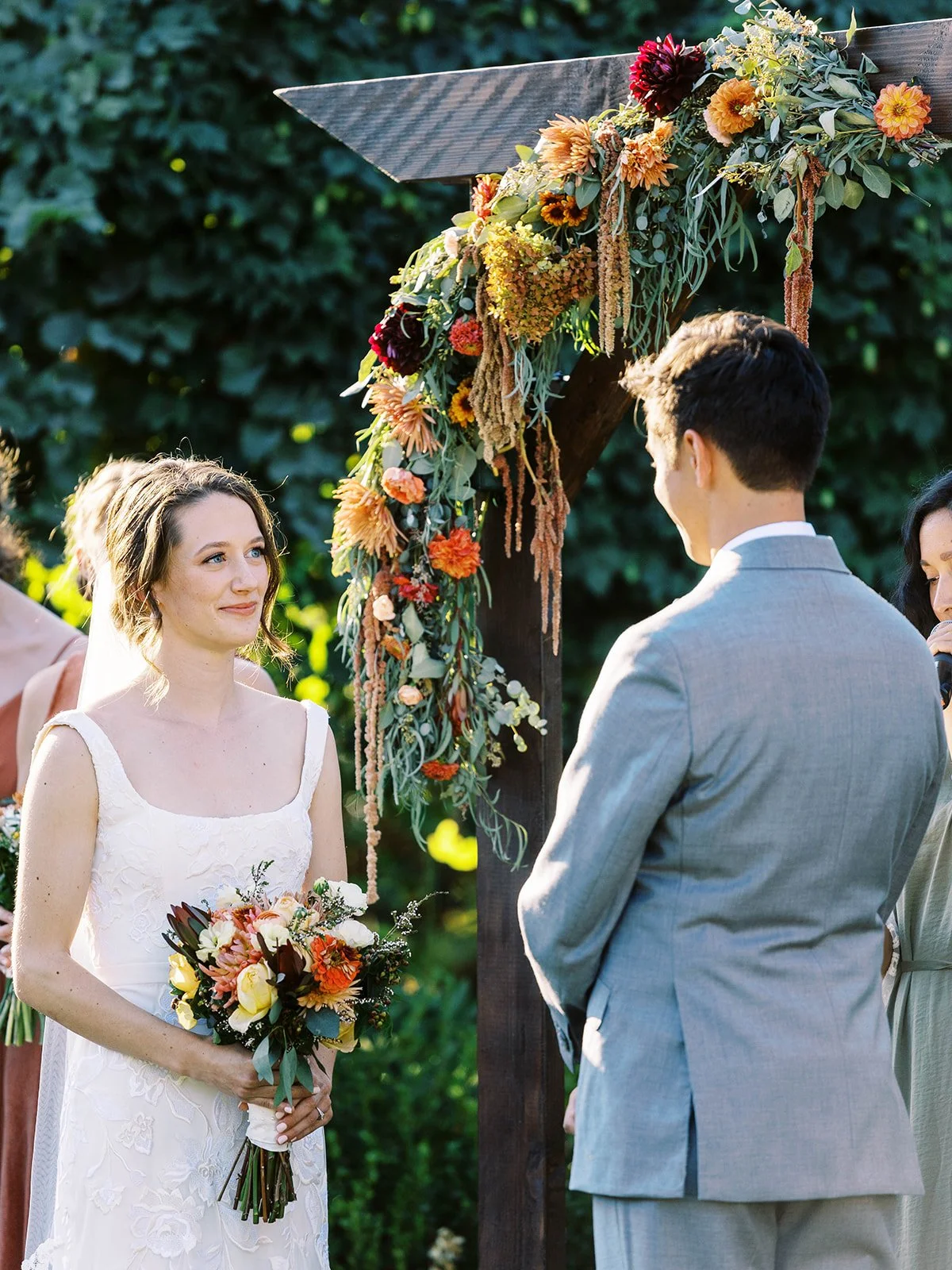 Bride and groom exchanging vows under floral arch, wedding party standing beside them