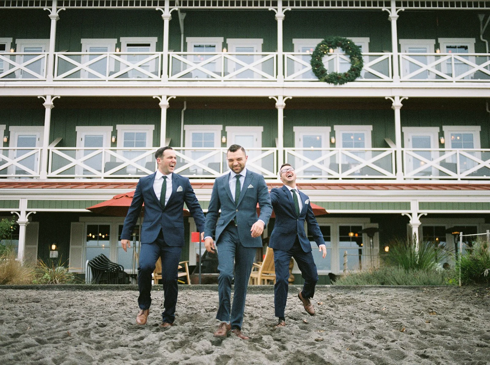 Groom and two groomsmen walk across the sandy riverfront in blue suits during an Oregon wedding.