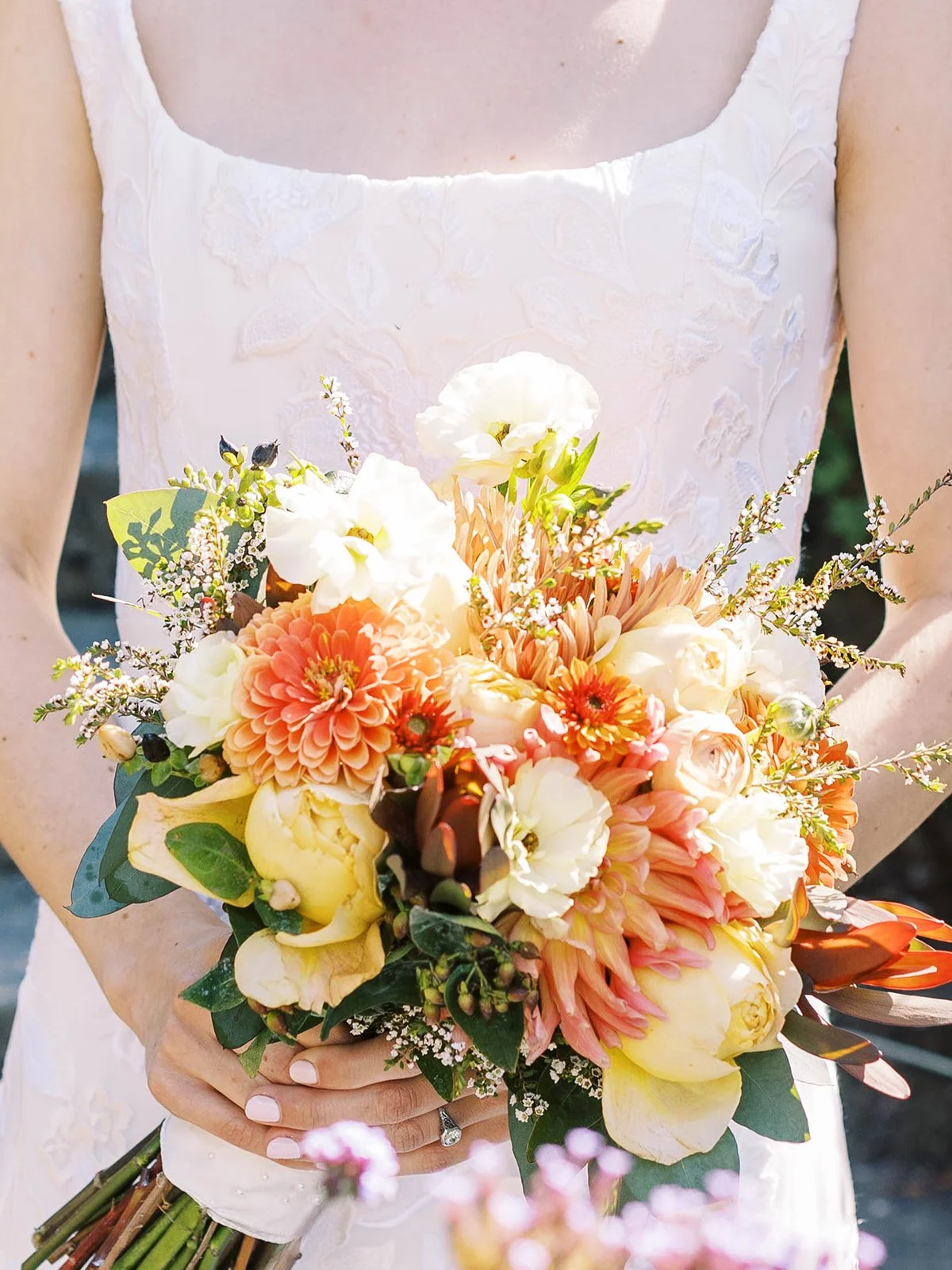 Bride holding a colorful bouquet of peach, cream and orange flowers against her white wedding dress.