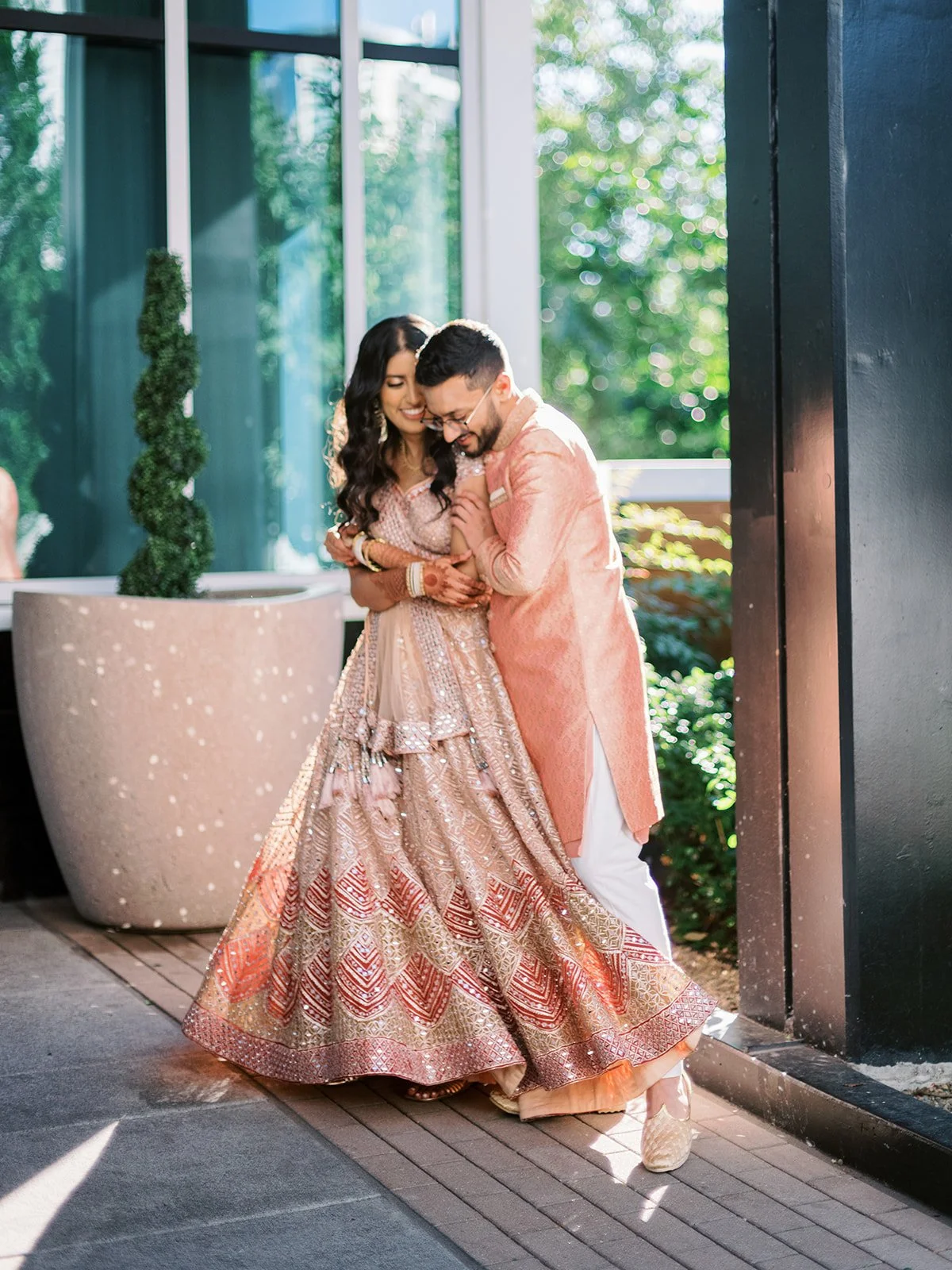 Couple in peach and gold traditional Indian attire walking together outdoors in soft evening light.
