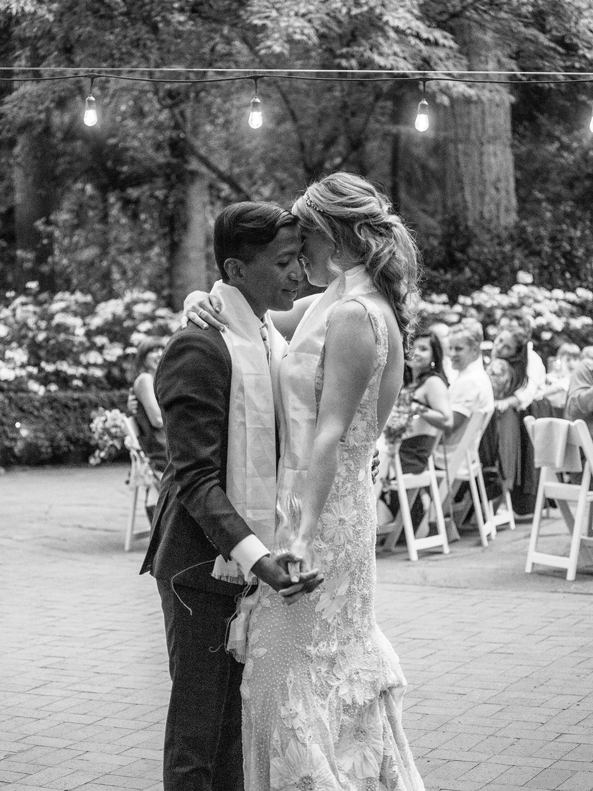 Bride and groom lean close during their first dance beneath glowing string lights.