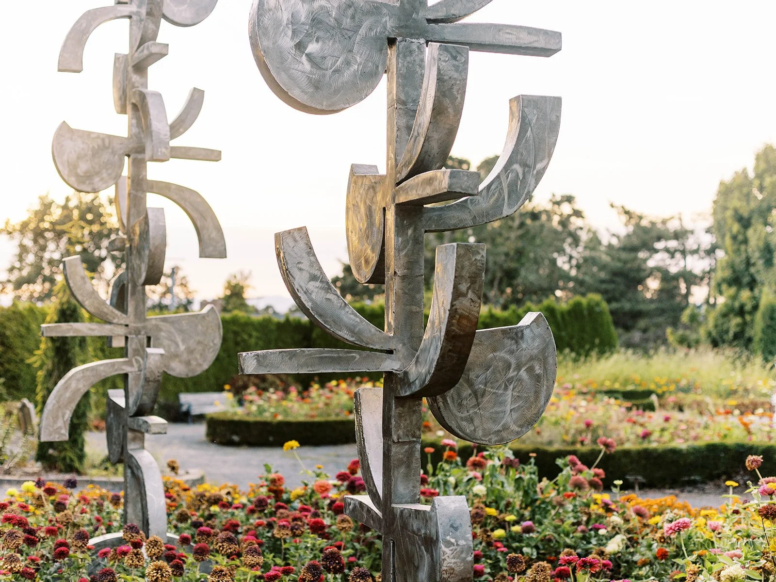 Modern metal sculptures displayed in a colorful flower garden at sunset