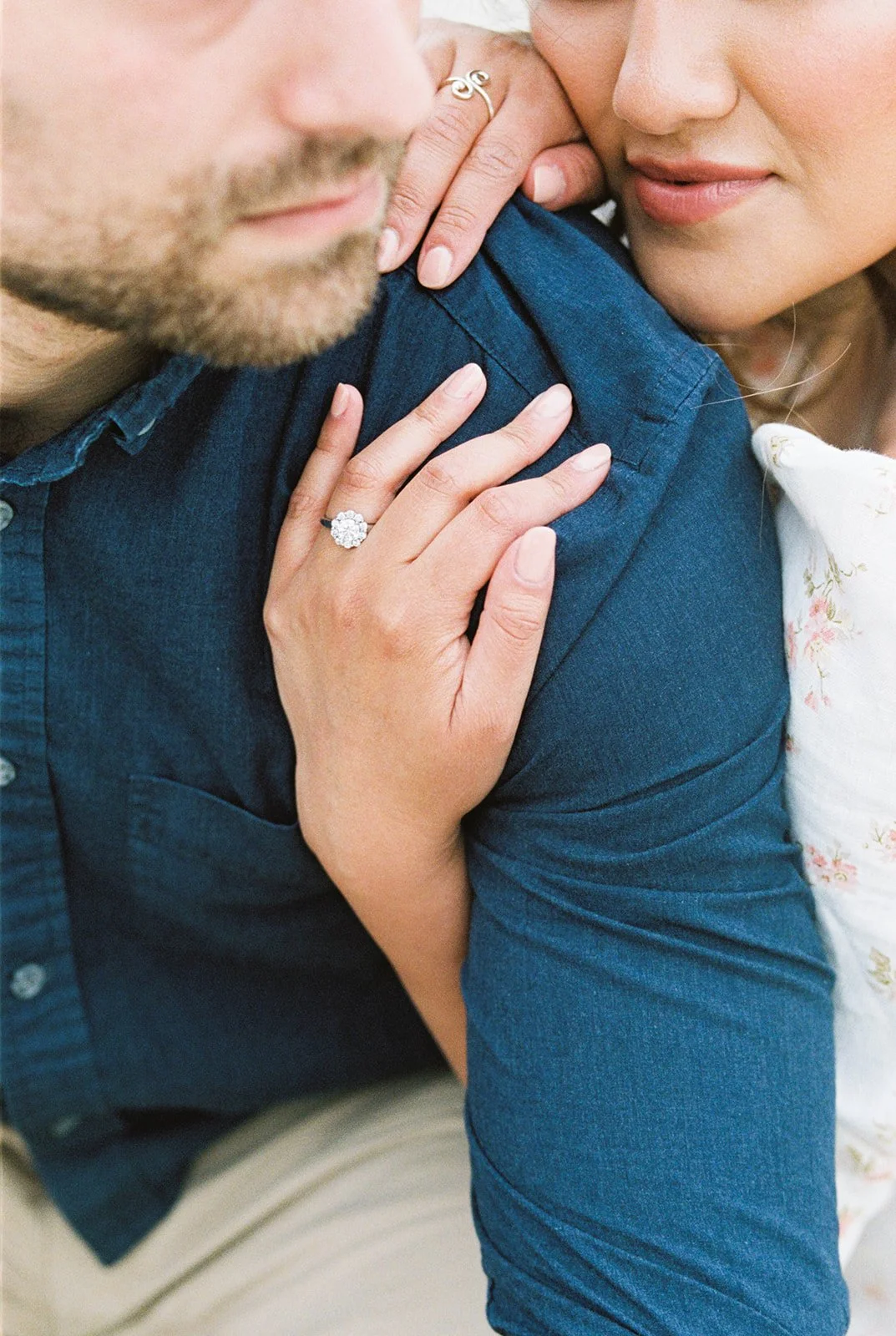 Detail shot of engagement ring on woman’s hand resting on man’s shoulder
