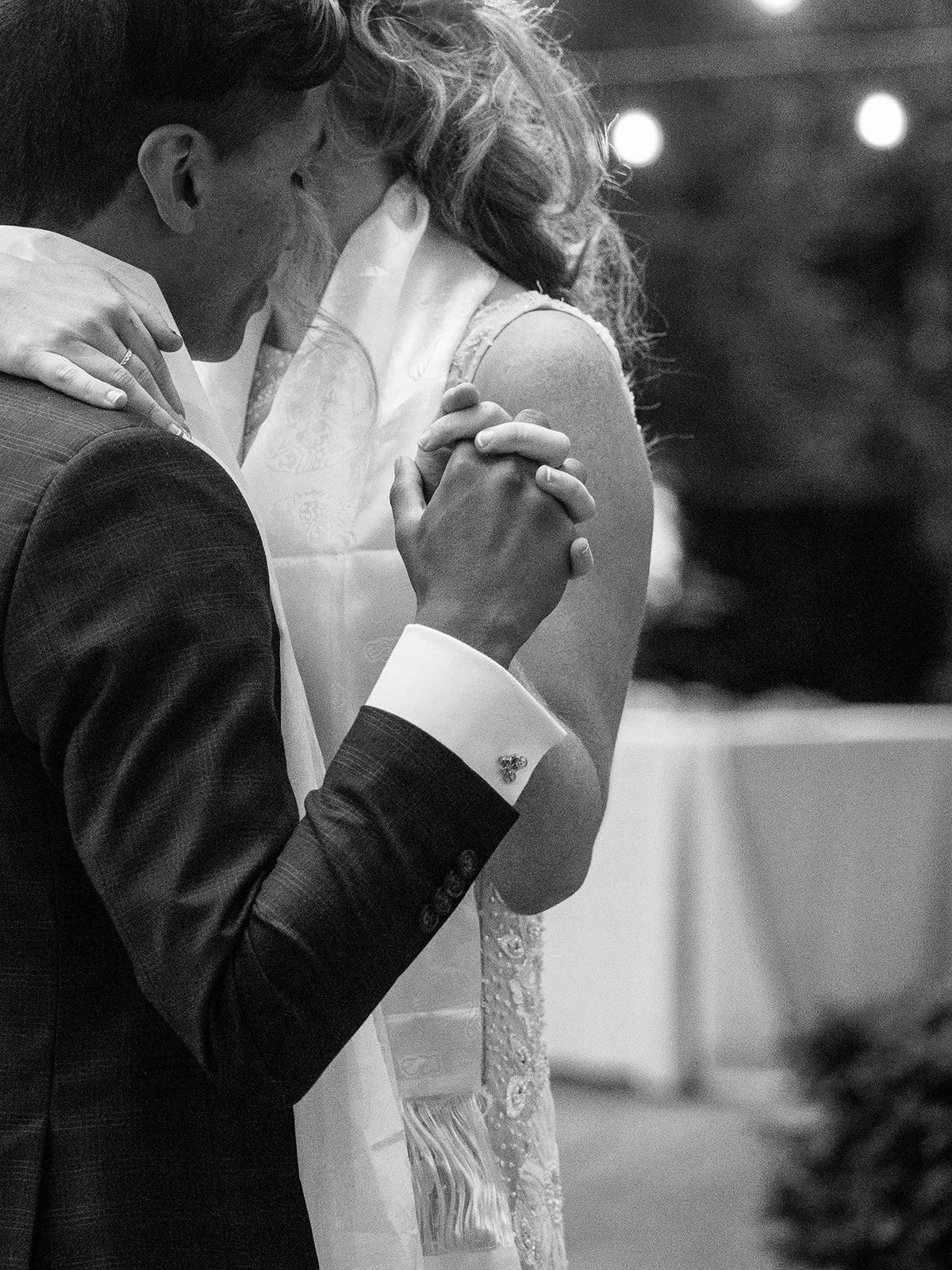 Black-and-white close-up of the newlyweds holding hands during their first dance.