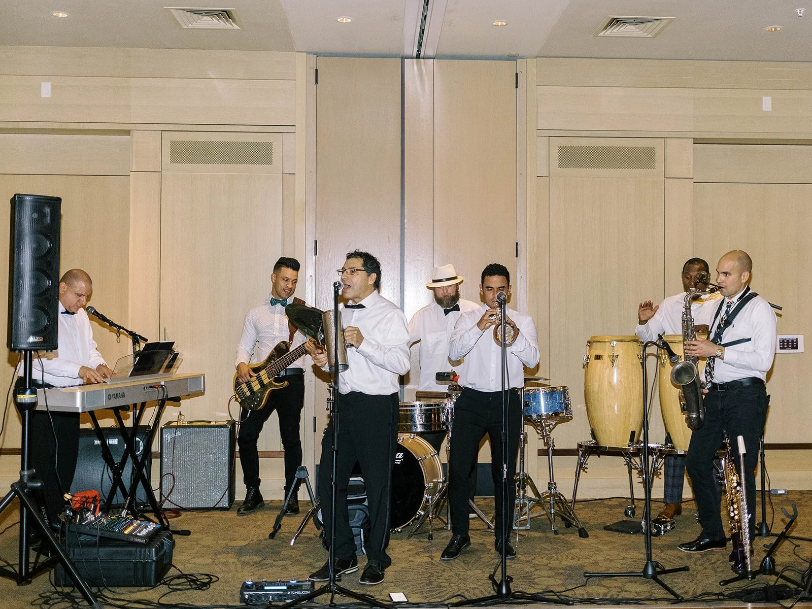 Full live band performing at the wedding reception, featuring keyboard, bass guitar, vocalist, trumpet, congas, and saxophone