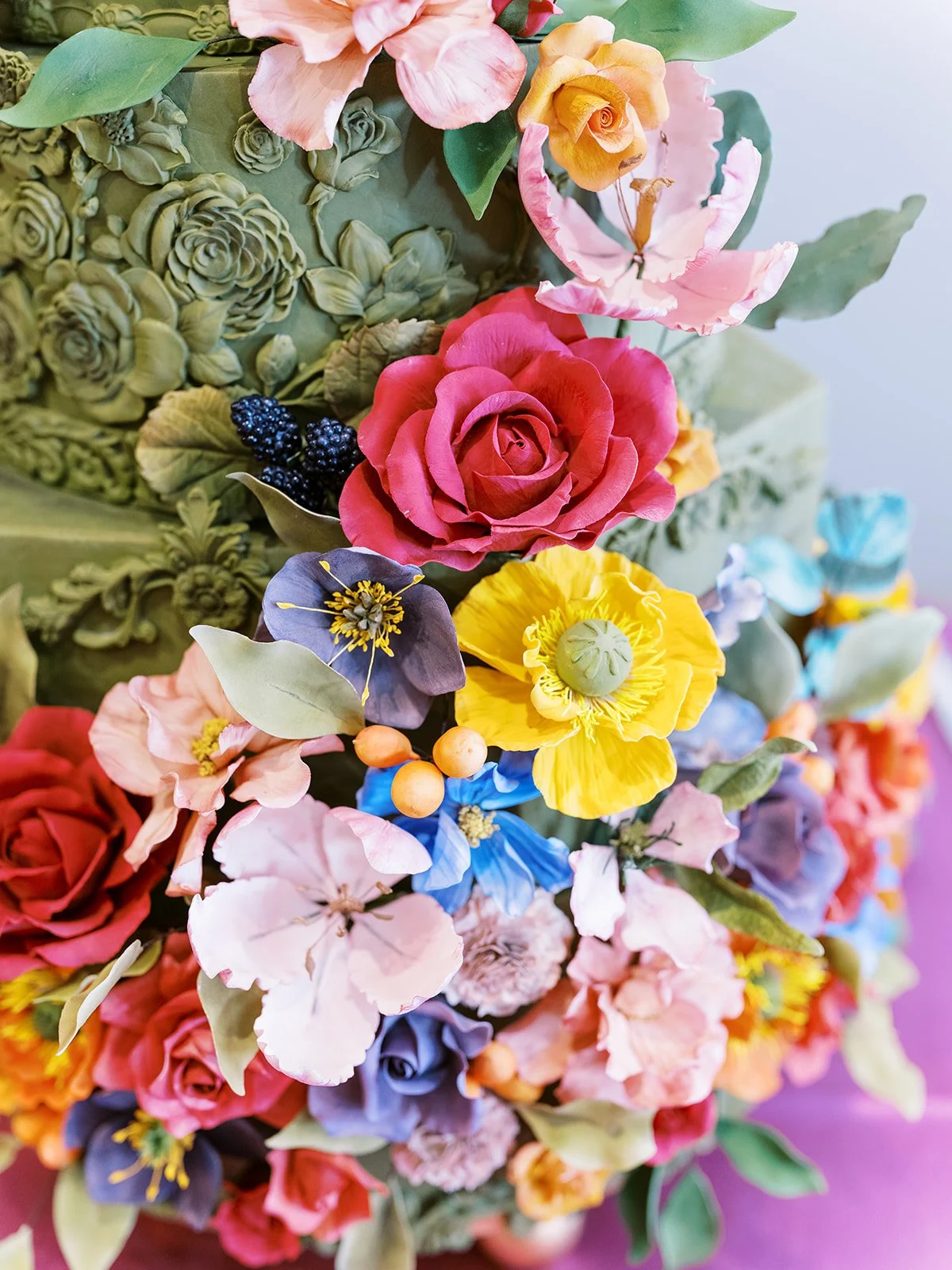 Intricate green wedding cake with ornate floral patterns and colorful sugar flowers in pink, yellow, and blue.