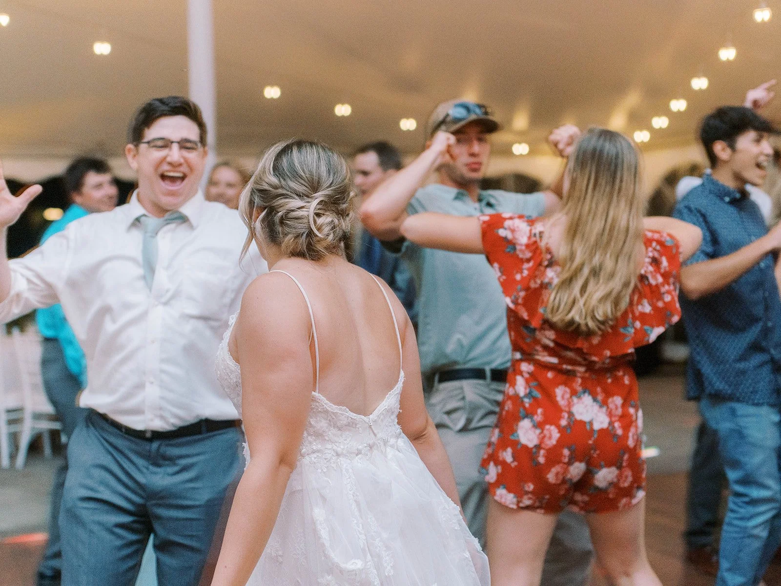 Bride dances with wedding guests under a reception tent, surrounded by friends celebrating on the dance floor.