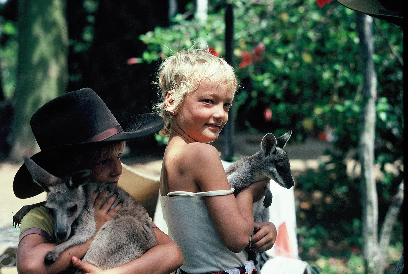 Two children holding puppies outdoors among trees and greenery in a vintage family photograph.