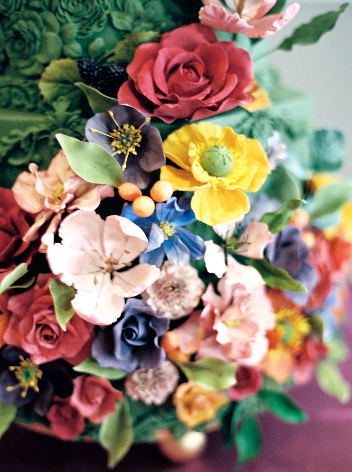 Close-up of colorful sugar flowers on a textured green cake with shallow depth of field and soft pastel tones.