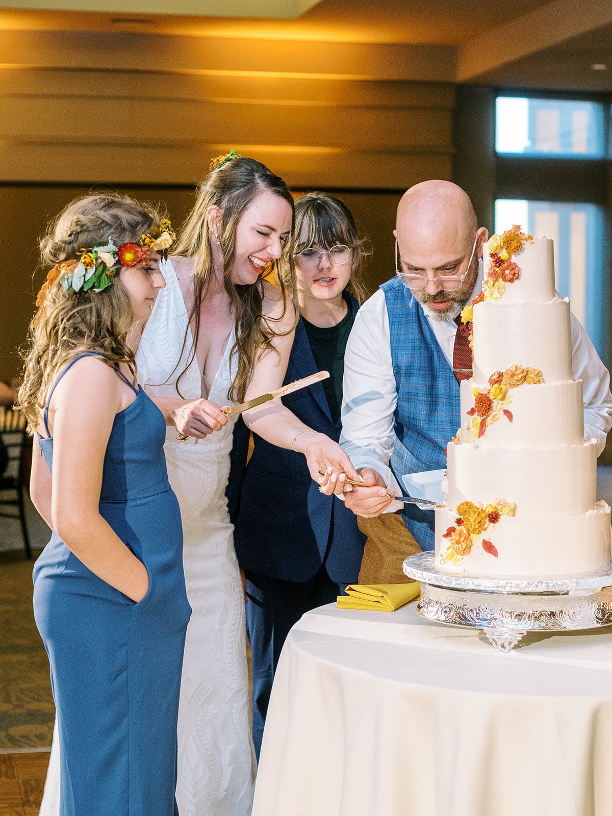 Bride and groom cutting their floral wedding cake with two attendants standing beside them.