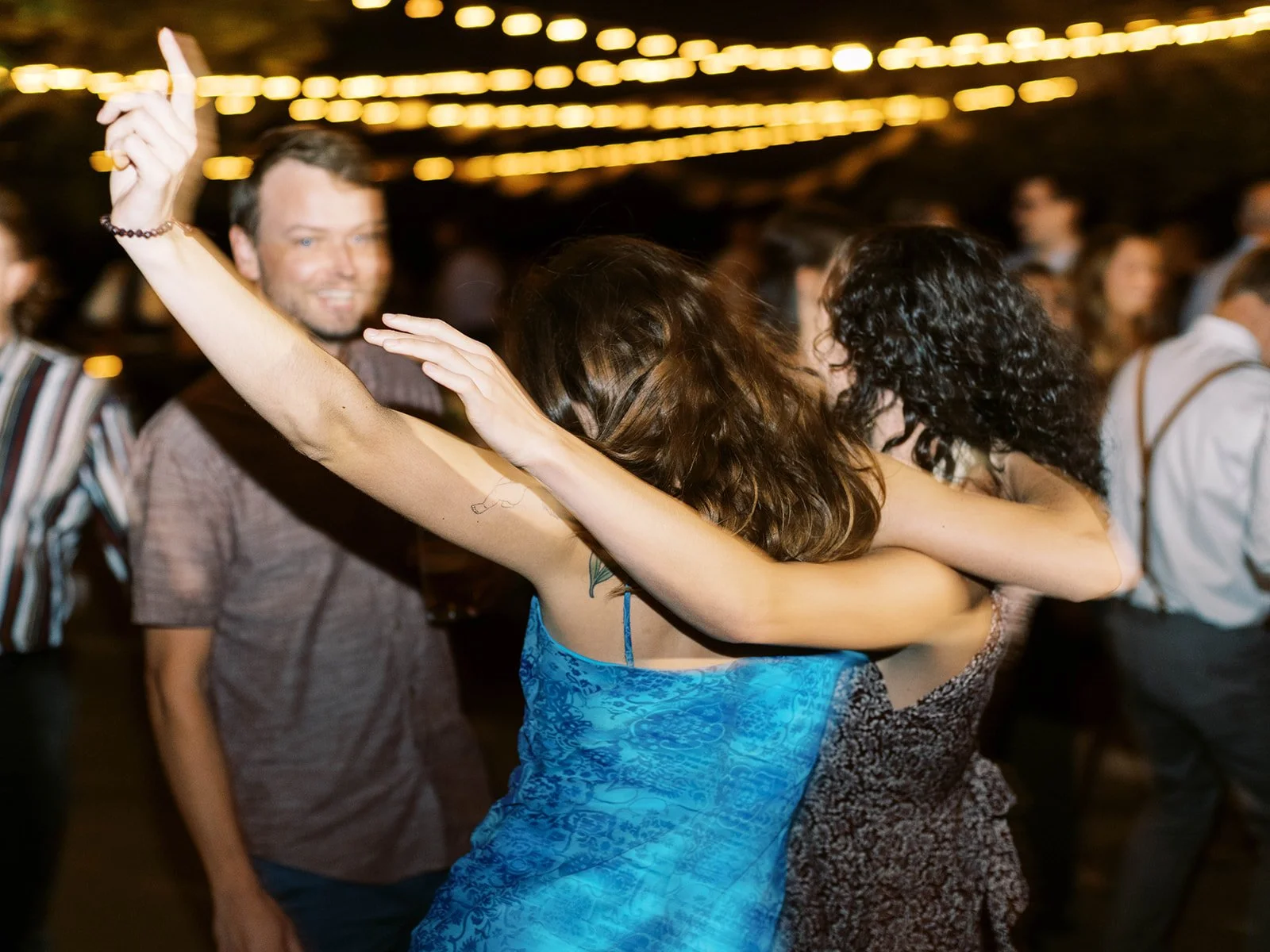 Wedding guests dancing with arms around each other under string lights at outdoor reception